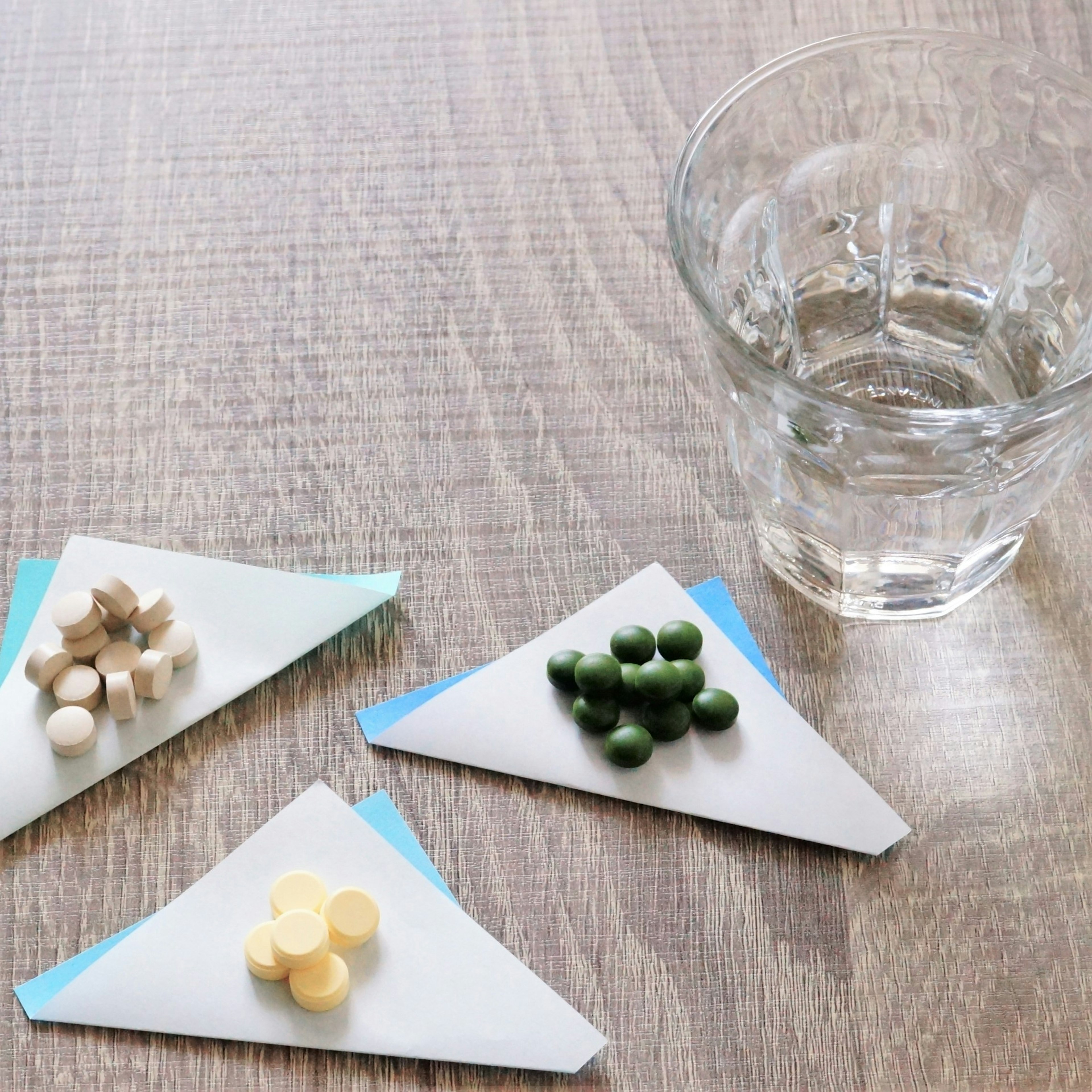 Different colored tablets arranged on triangular paper next to a clear glass