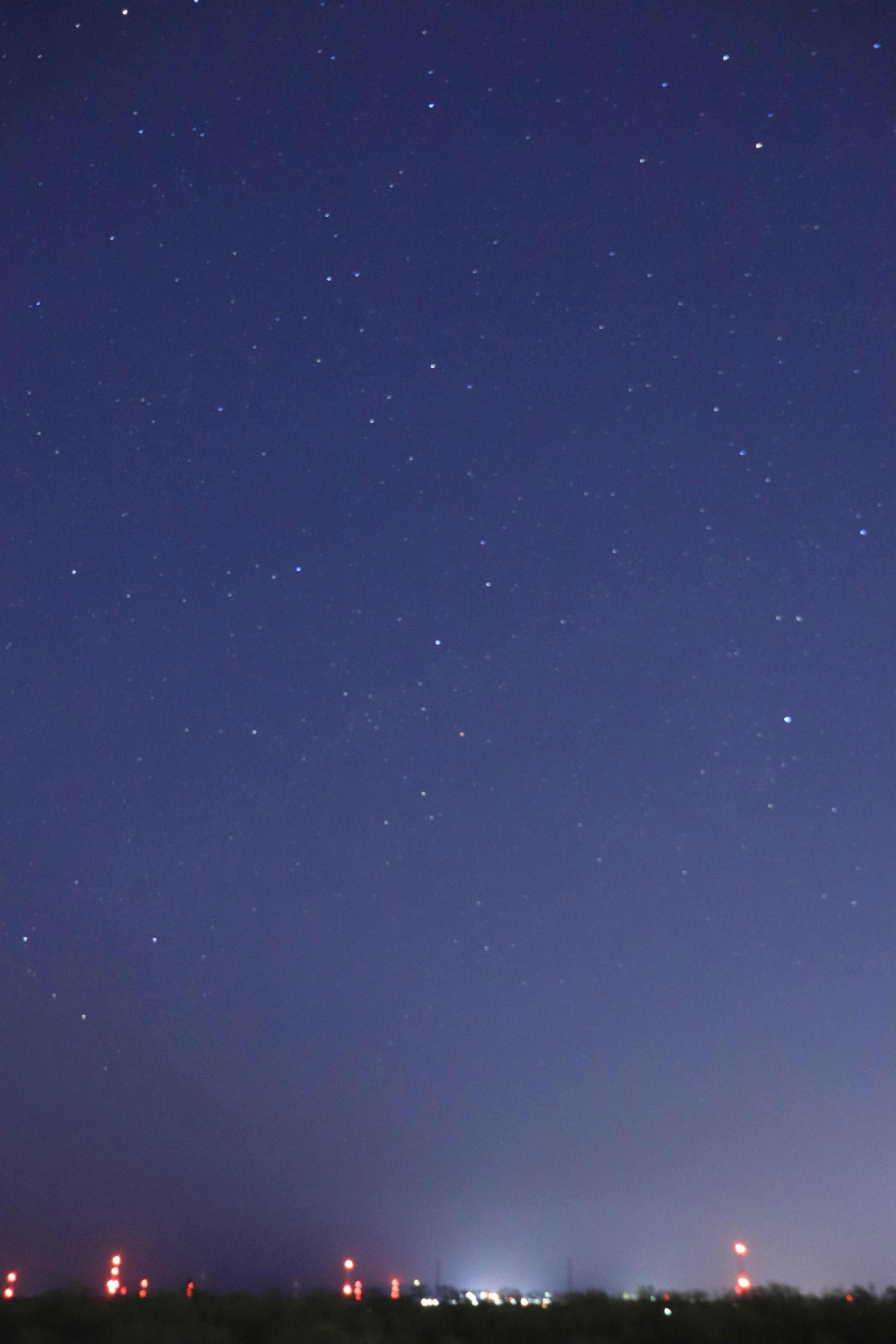 夜空に輝く星々と遠くの赤い灯台が見える風景