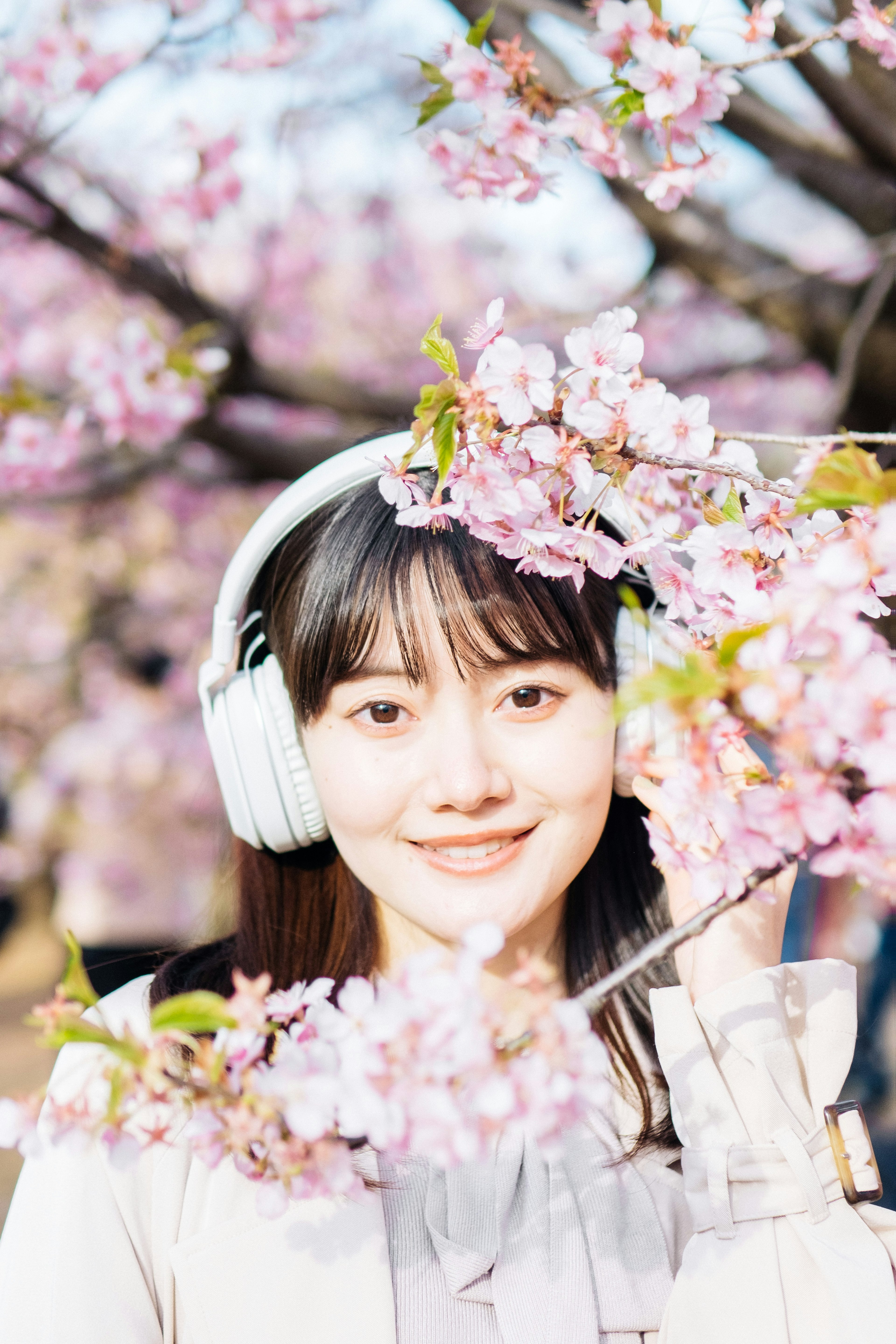 桜の花の間から微笑む女性がヘッドフォンをつけている