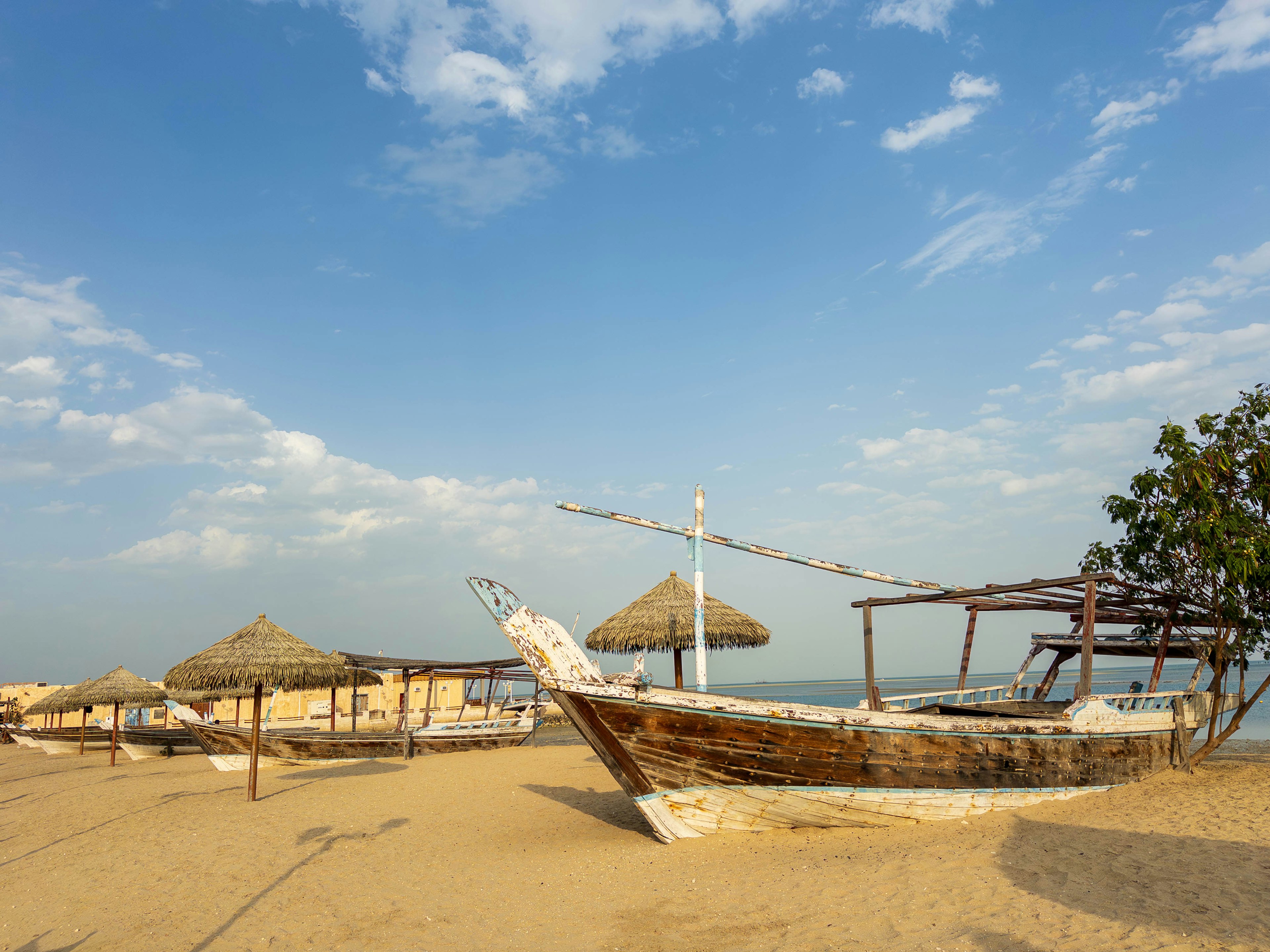 Old wooden boat on sandy beach with thatched huts and blue sky