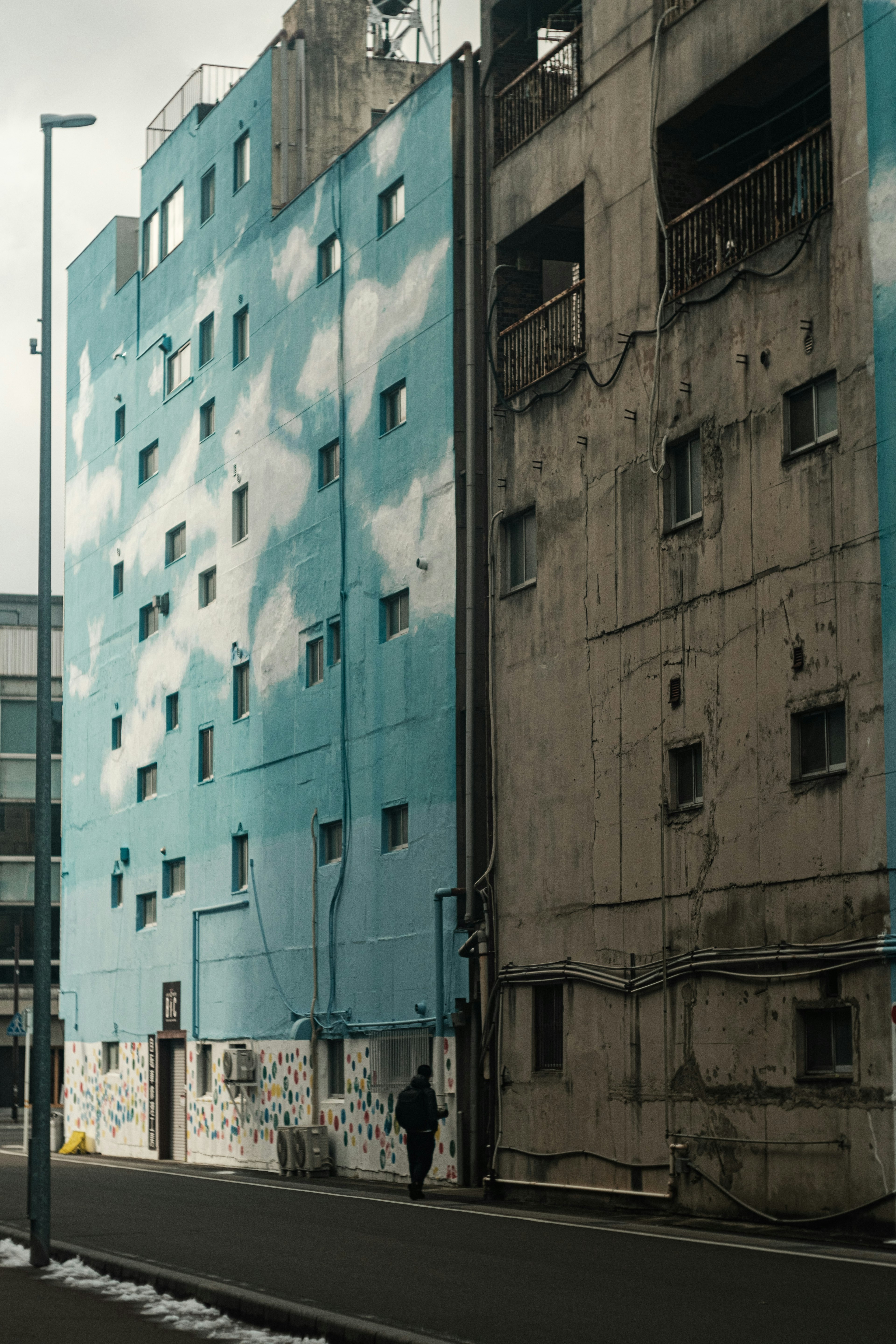 Scena urbana con un edificio blu con nuvole bianche e un vecchio edificio in cemento