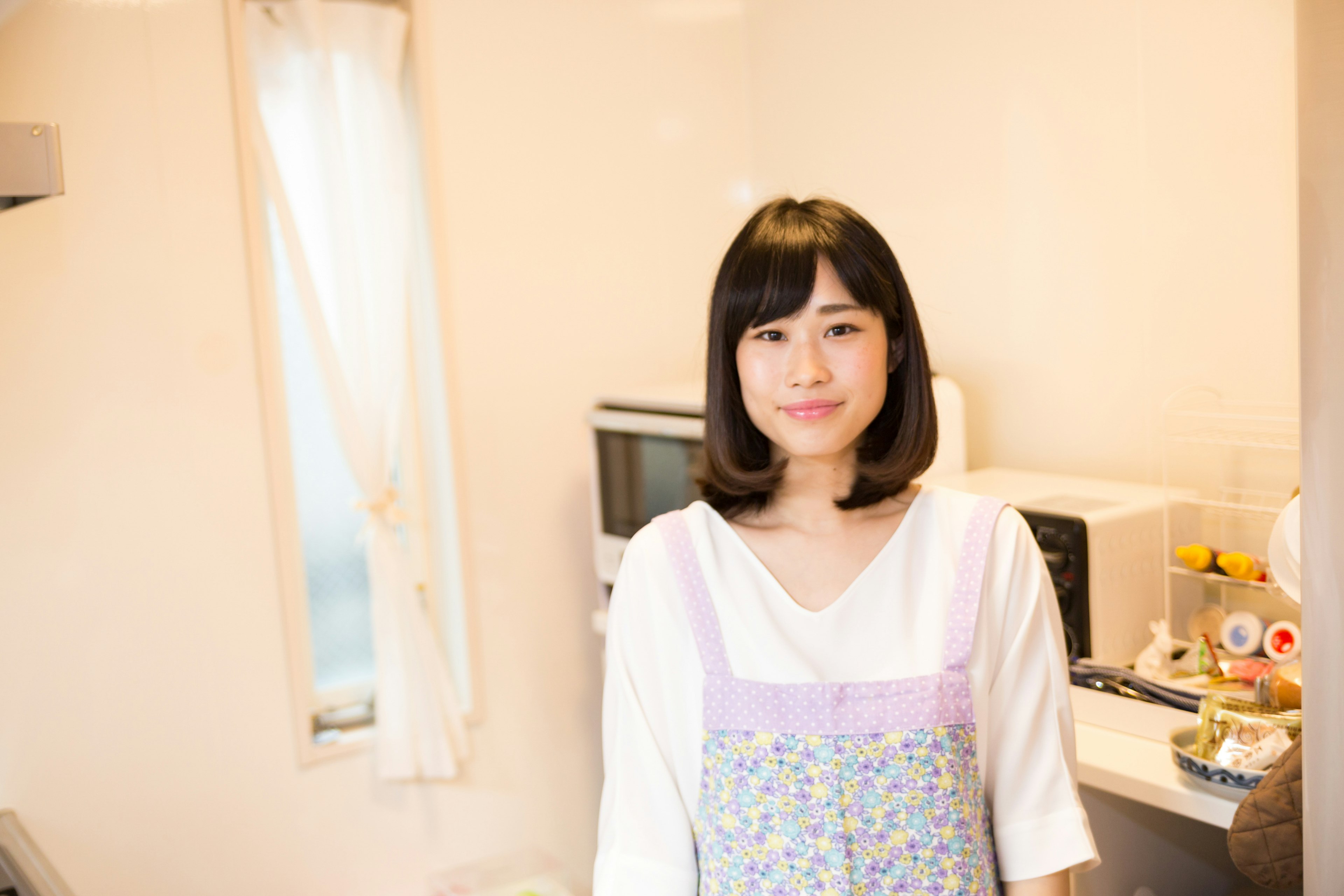 Una mujer sonriendo en una cocina con una blusa blanca y un delantal floral