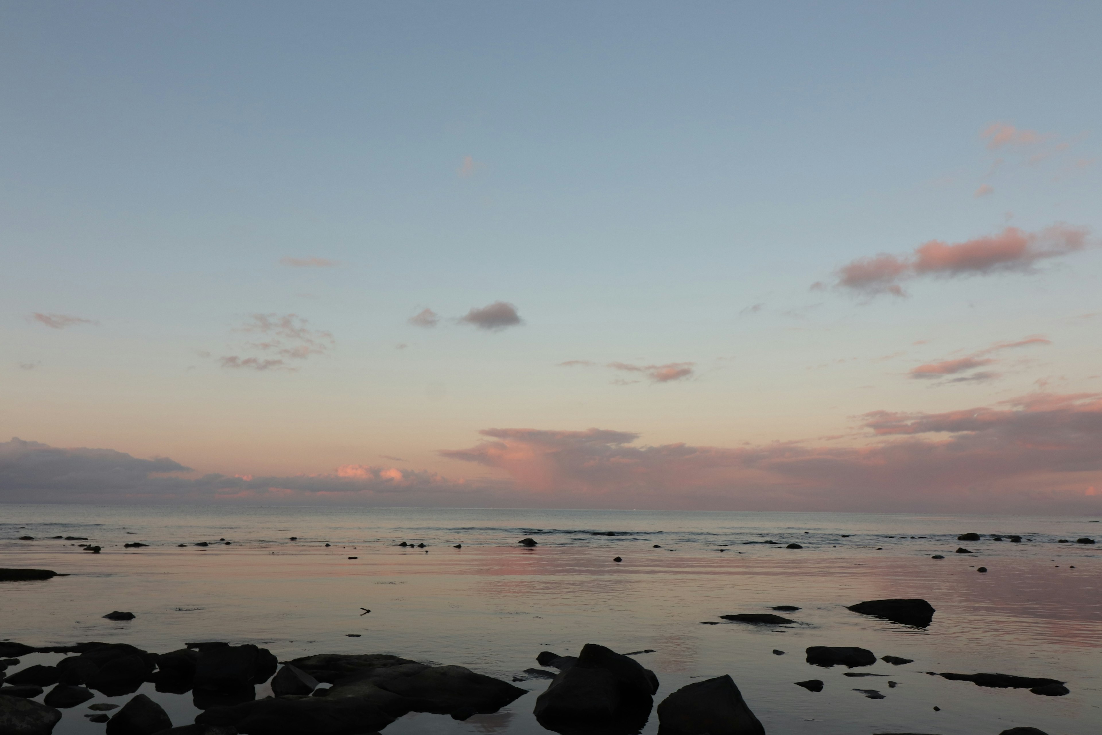 Pemandangan laut saat matahari terbenam dengan air yang cerah dan batu-batu yang terlihat