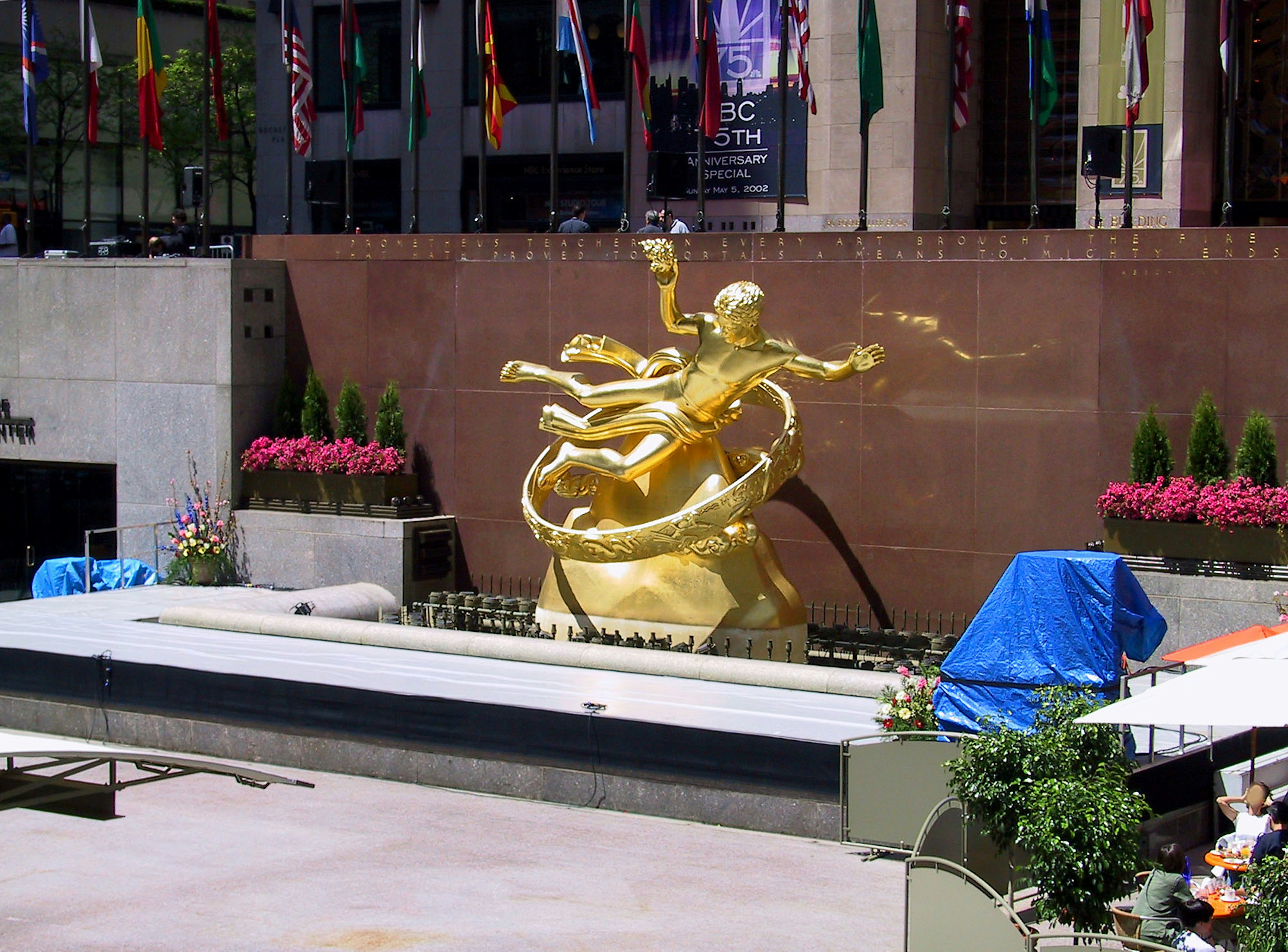 Golden sculpture at Rockefeller Center surrounded by flowers and flags