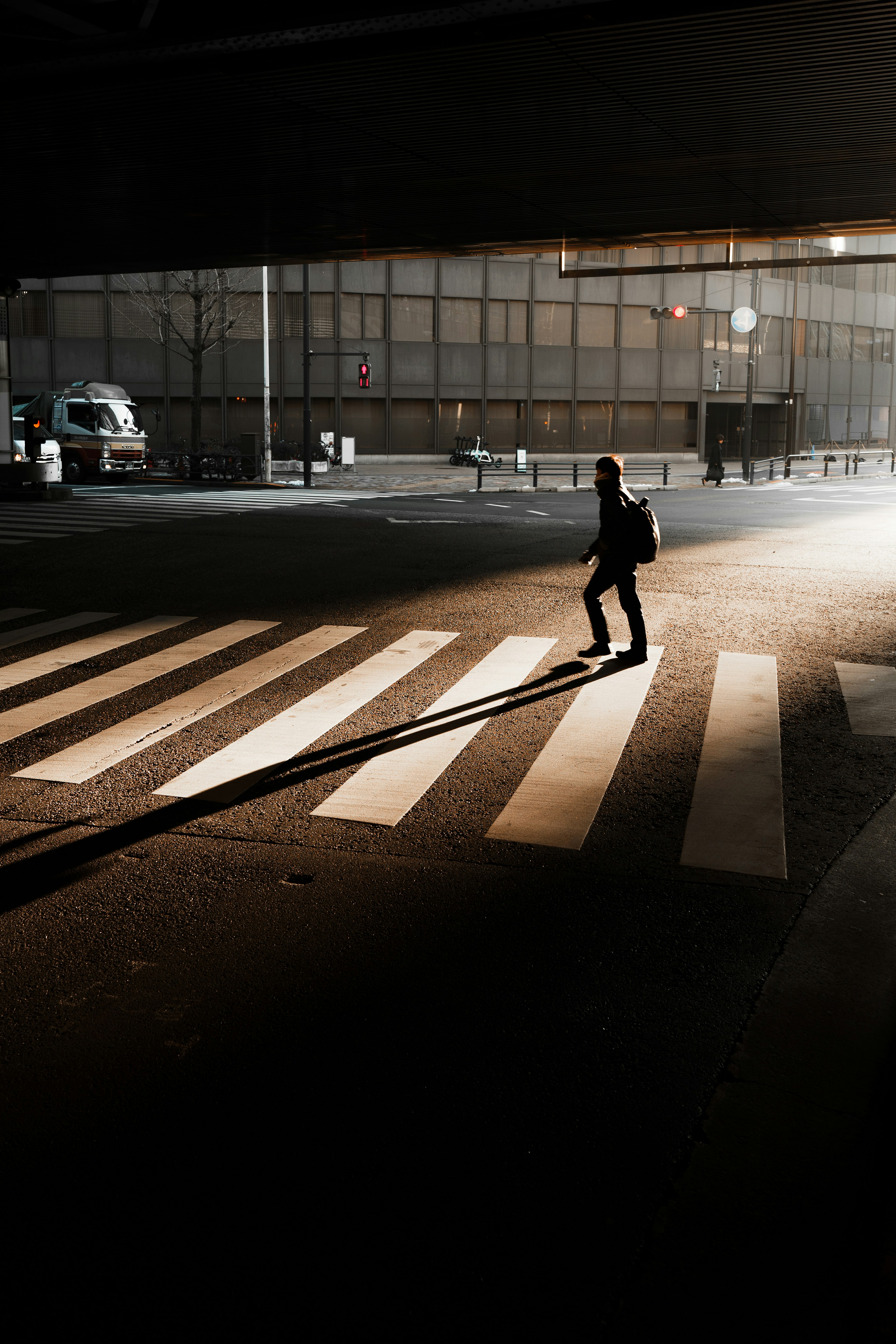 Silhouette di una persona che attraversa un attraversamento pedonale con lunghe ombre di notte