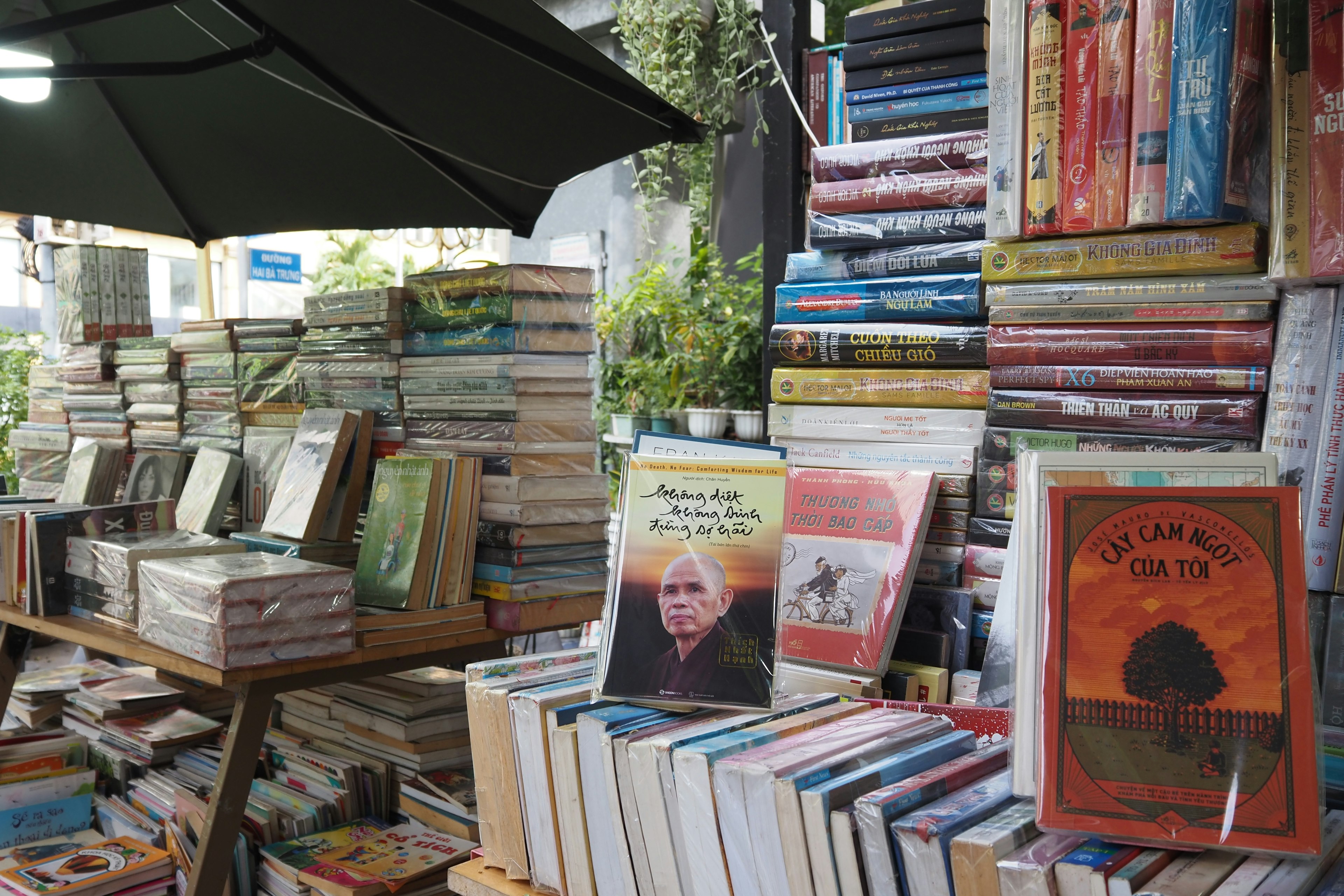 A collection of stacked books on display outside a bookstore under an umbrella