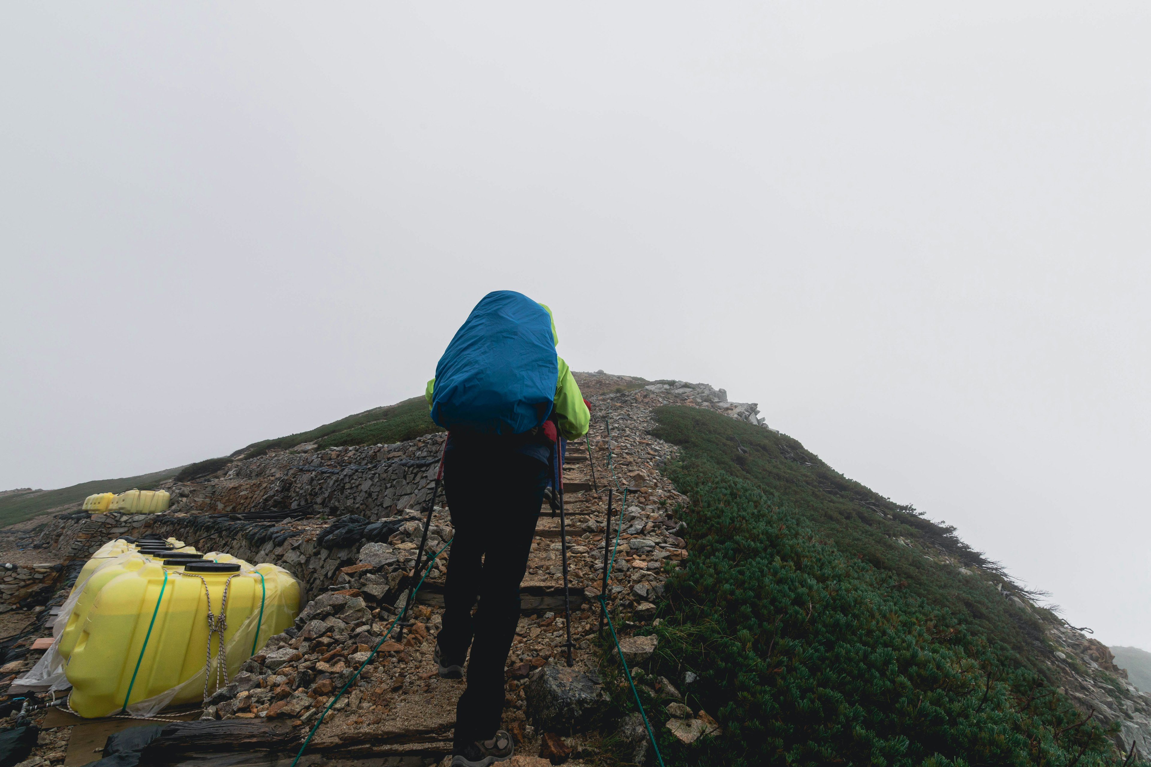 Wanderer, der einen felsigen Weg im Nebel mit einem bunten Rucksack hinaufsteigt