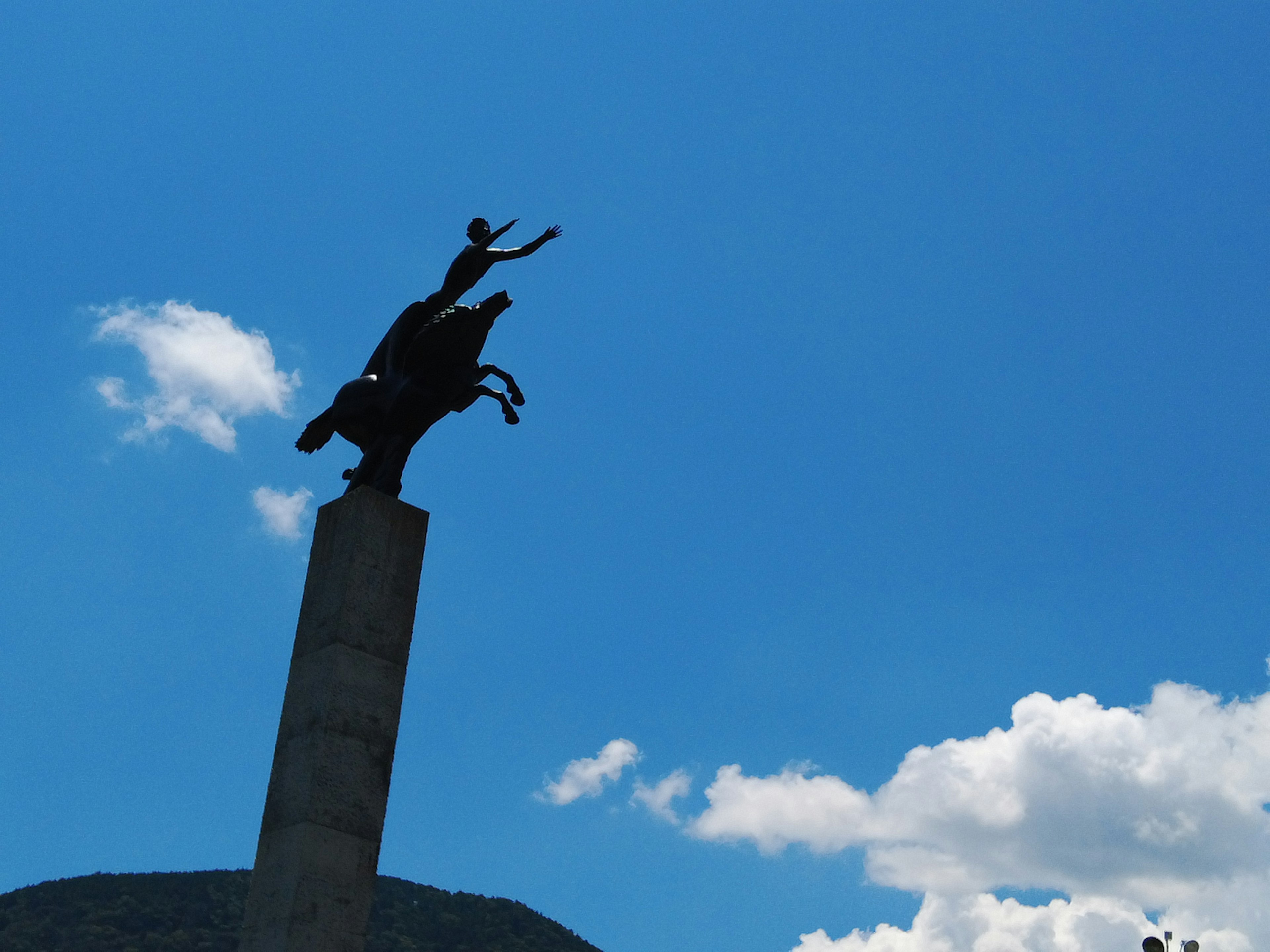 Silhouette of a horse statue against a blue sky with clouds