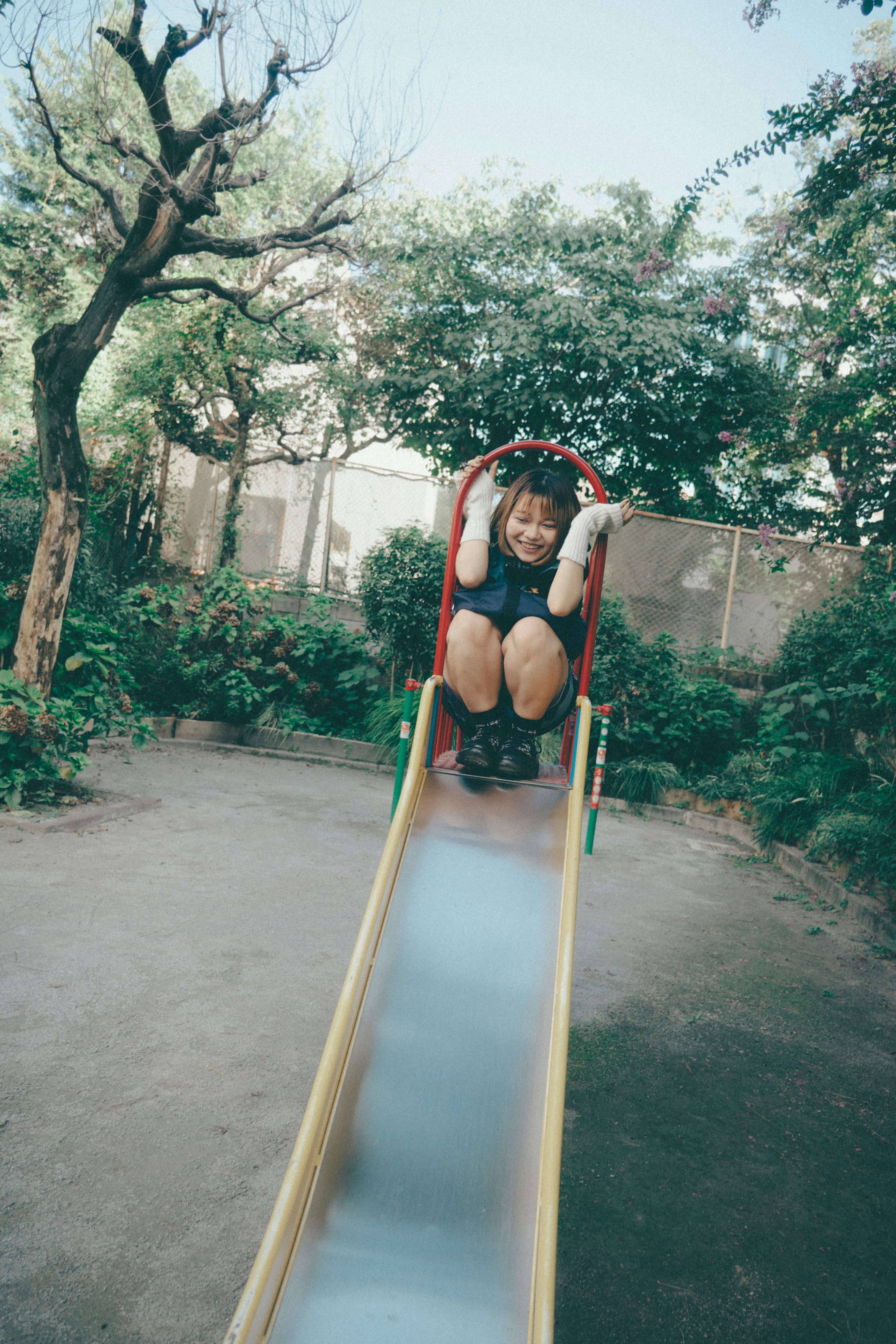 Child playing on a slide in a park with green trees and bushes in the background