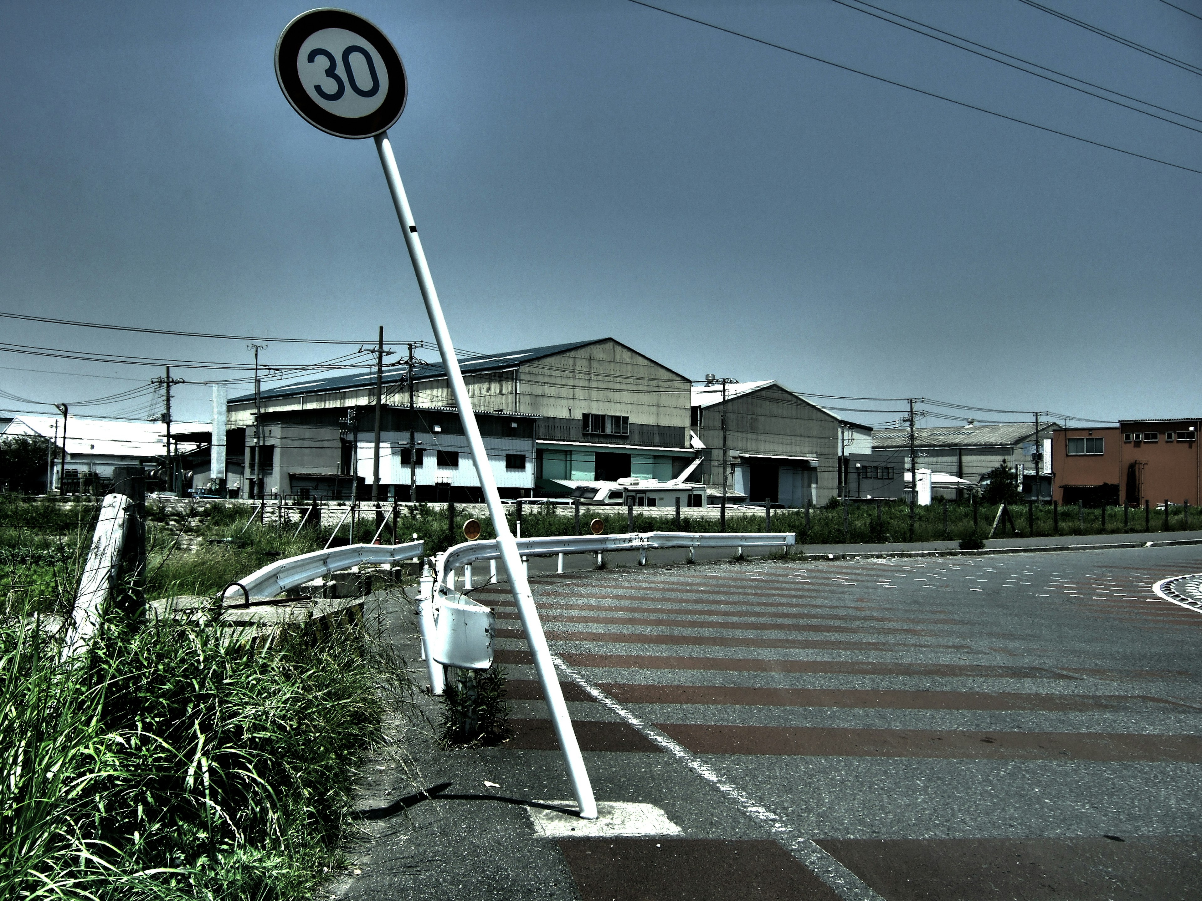 Panneau de limitation de vitesse de 30 km/h incliné avec des bâtiments industriels en arrière-plan