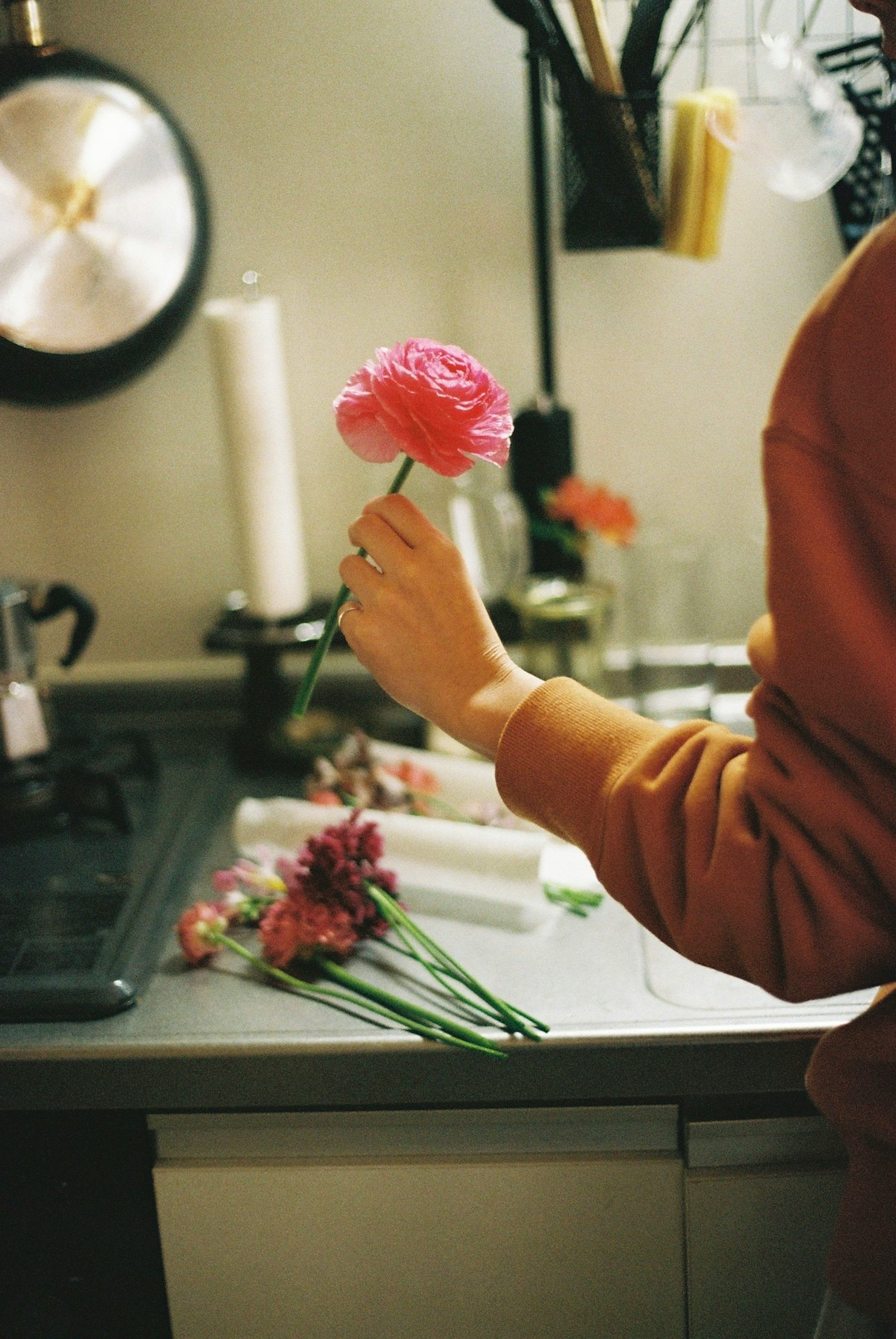 Une main tenant une fleur rose avec diverses fleurs sur un plan de travail de cuisine