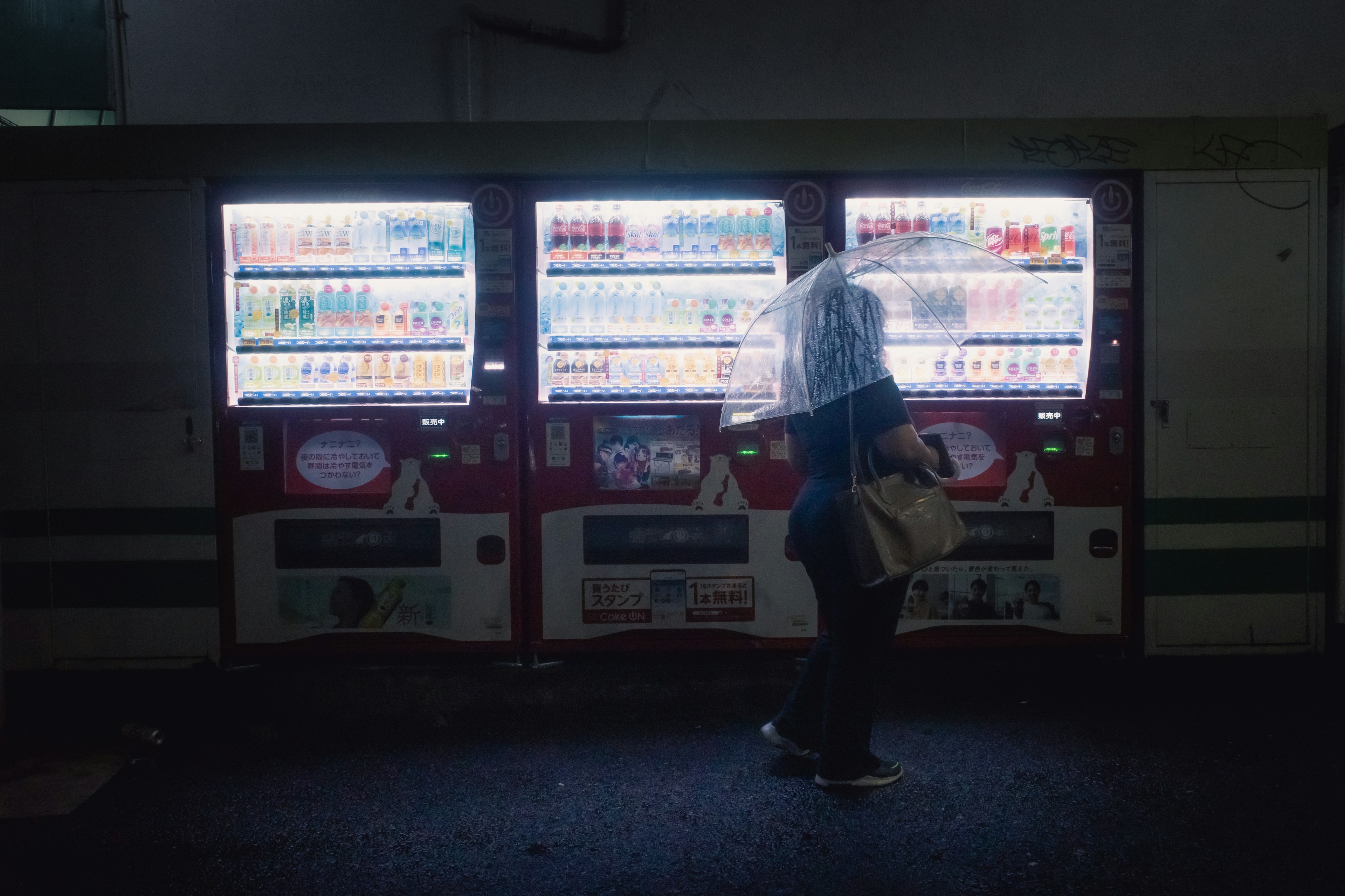 Silhouette of a person with an umbrella standing in front of vending machines