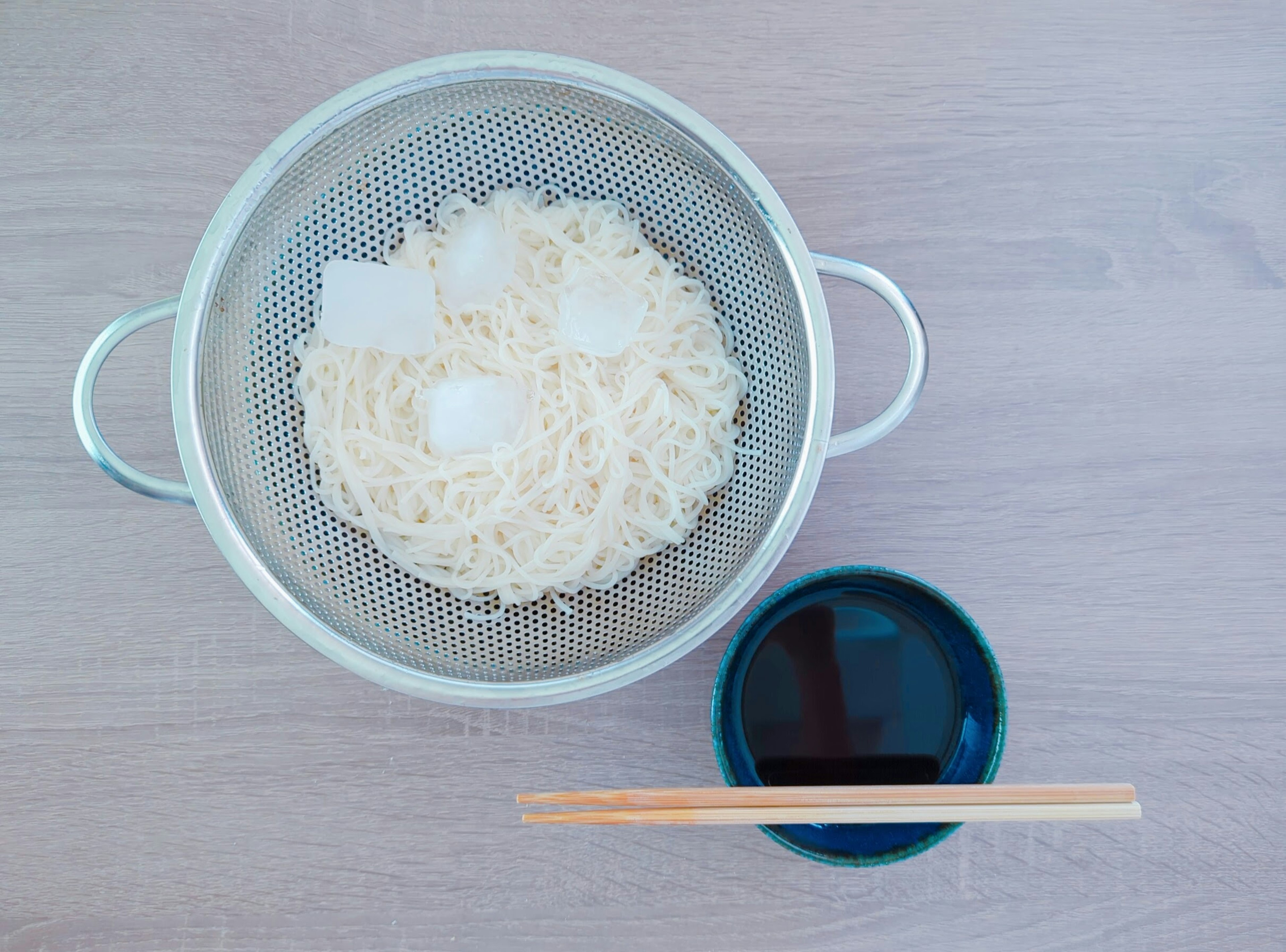 Chilled noodles in a sieve with a bowl of dipping sauce