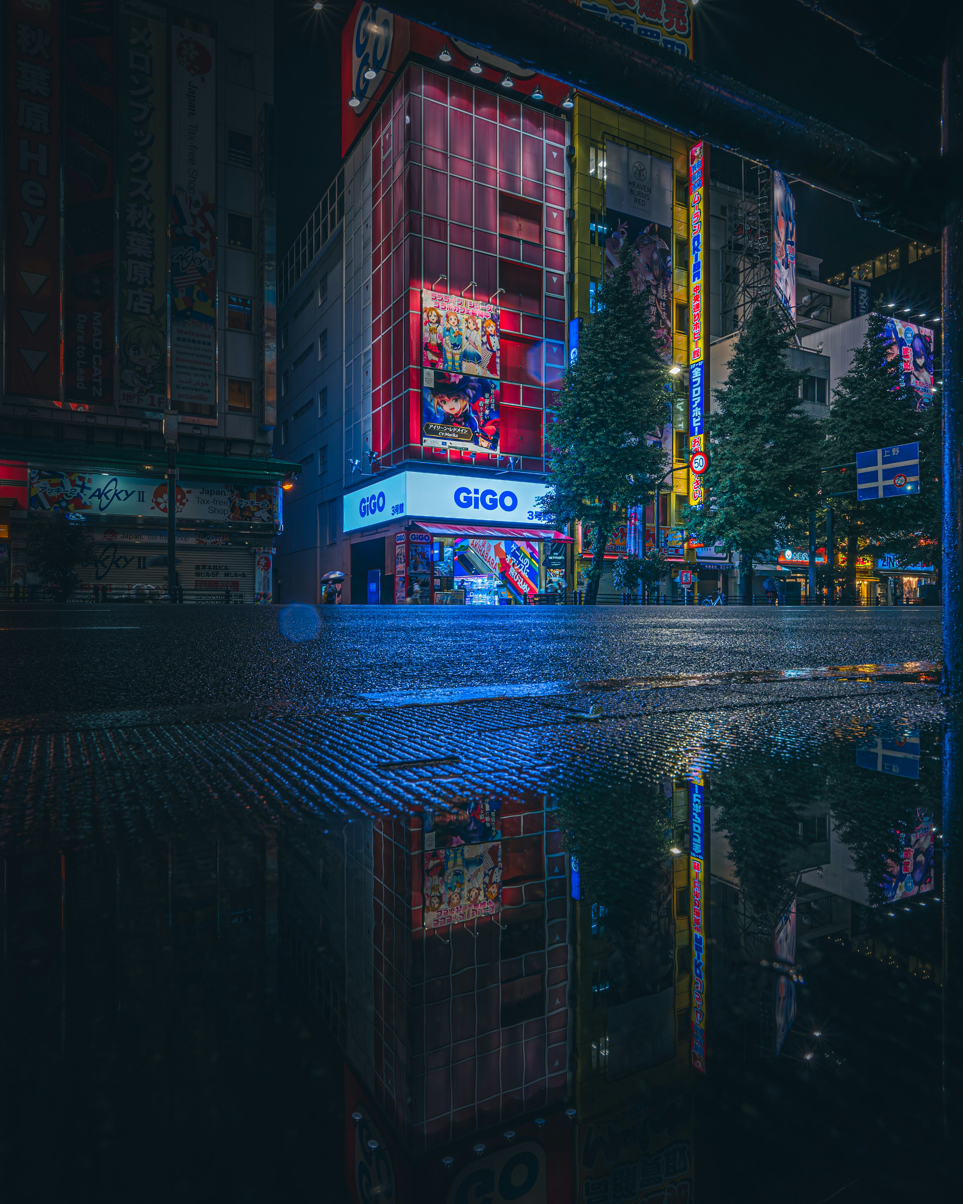 夜の街並みと青いネオンの反射が映る雨上がりの道路