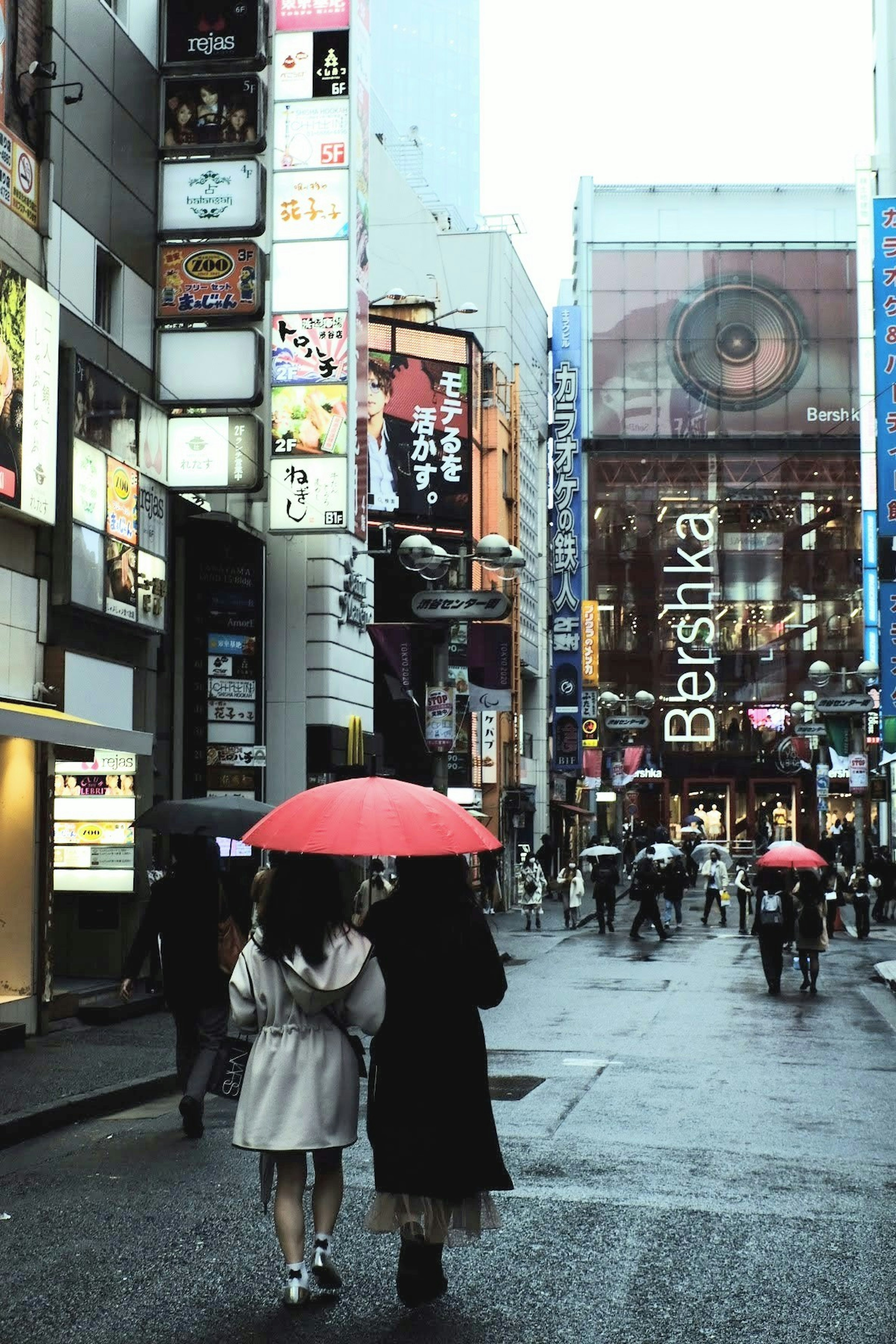 雨の中、赤い傘を持つ二人の女性が街を歩いています