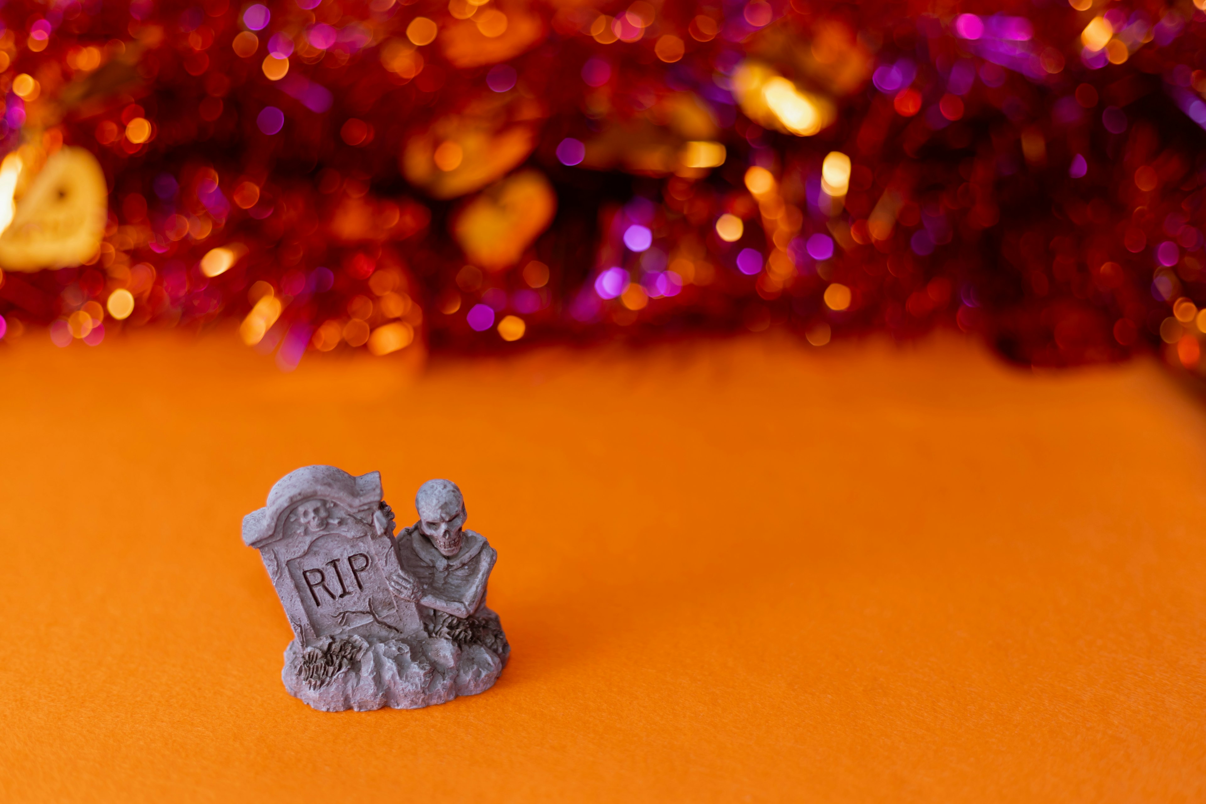 A small gravestone with RIP inscription and a figure kneeling beside it on an orange background