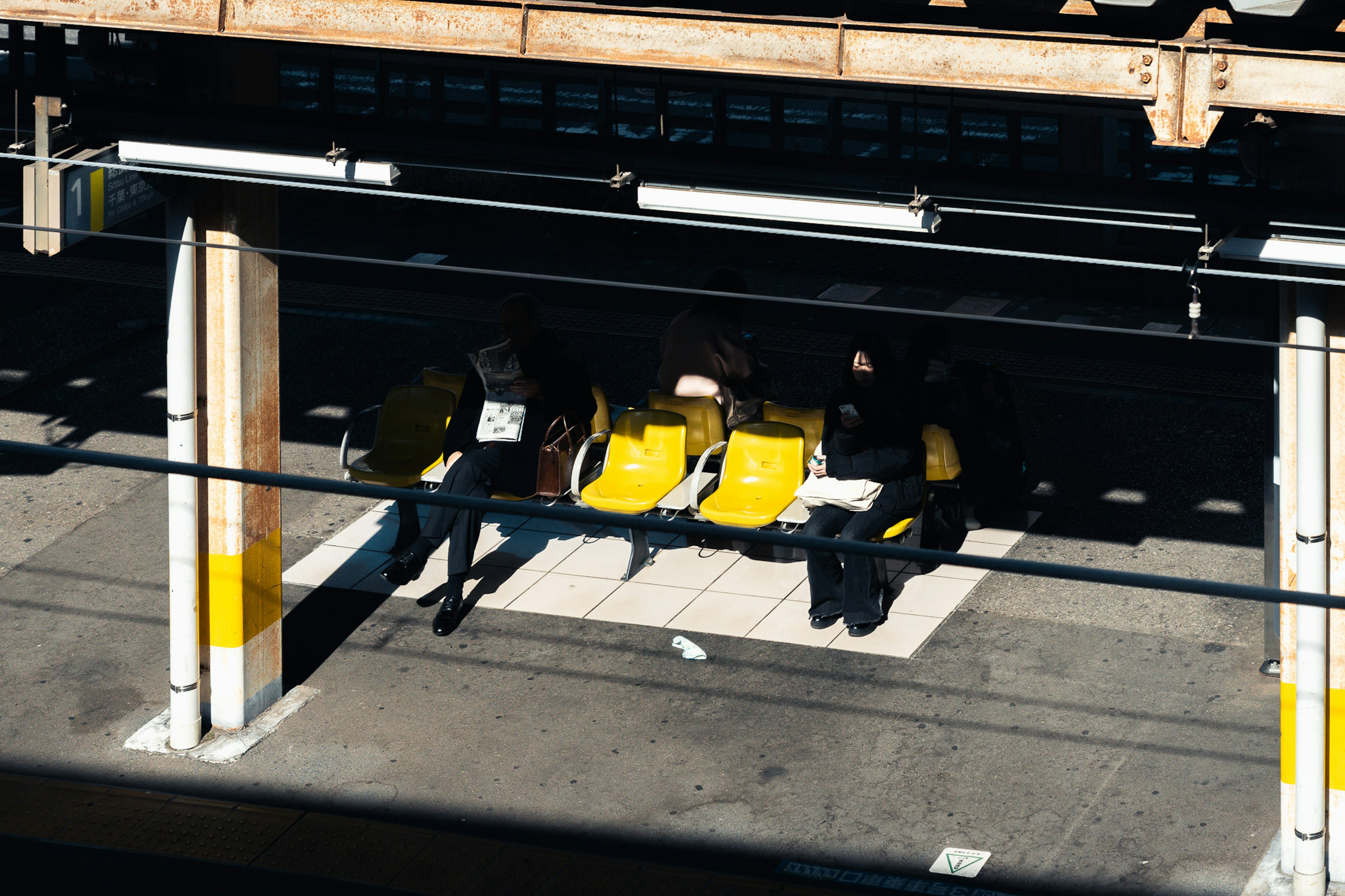 駅のプラットフォームに座る黄色い椅子と人々