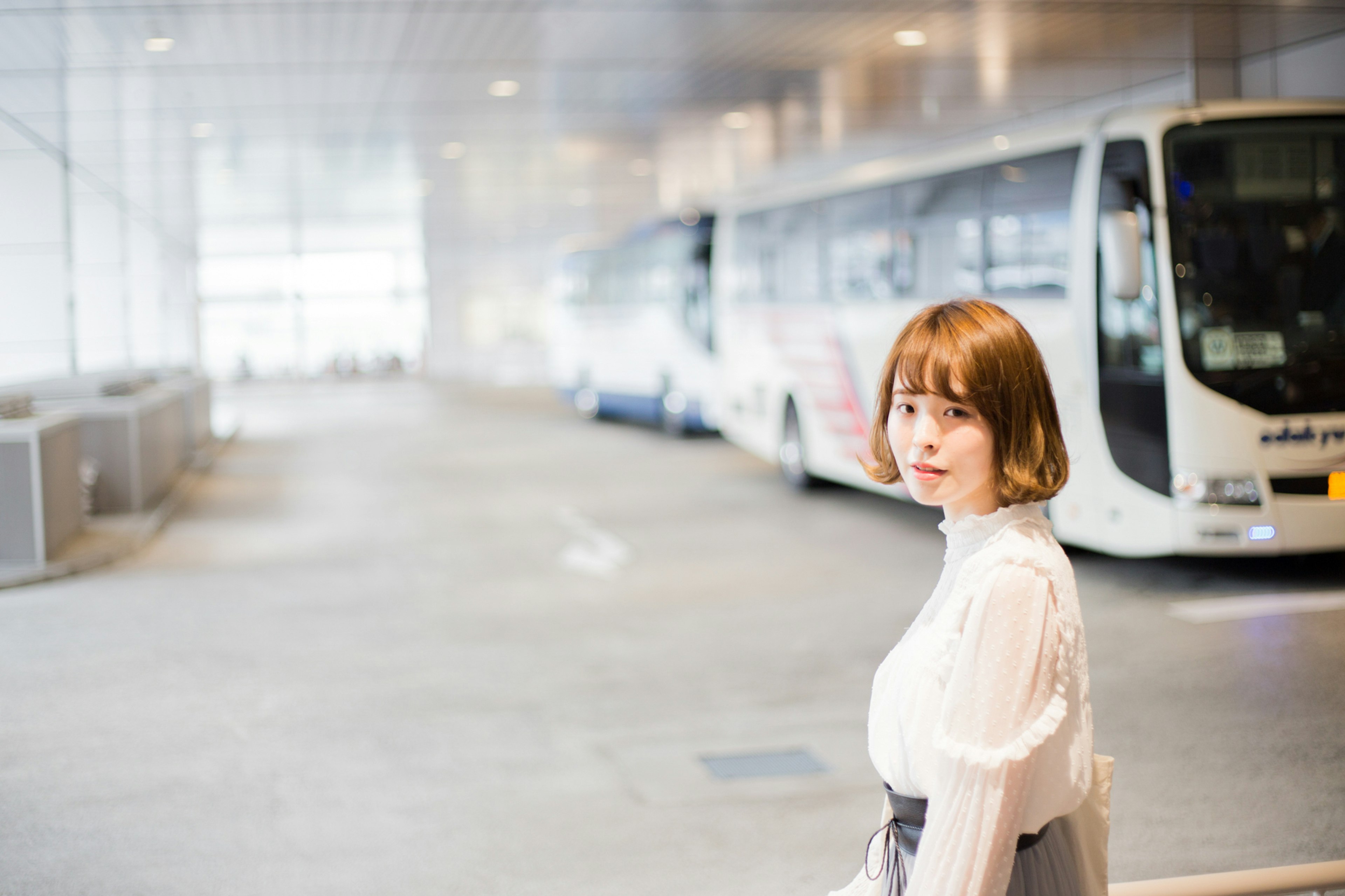 A woman in a white blouse looking back at a bus station