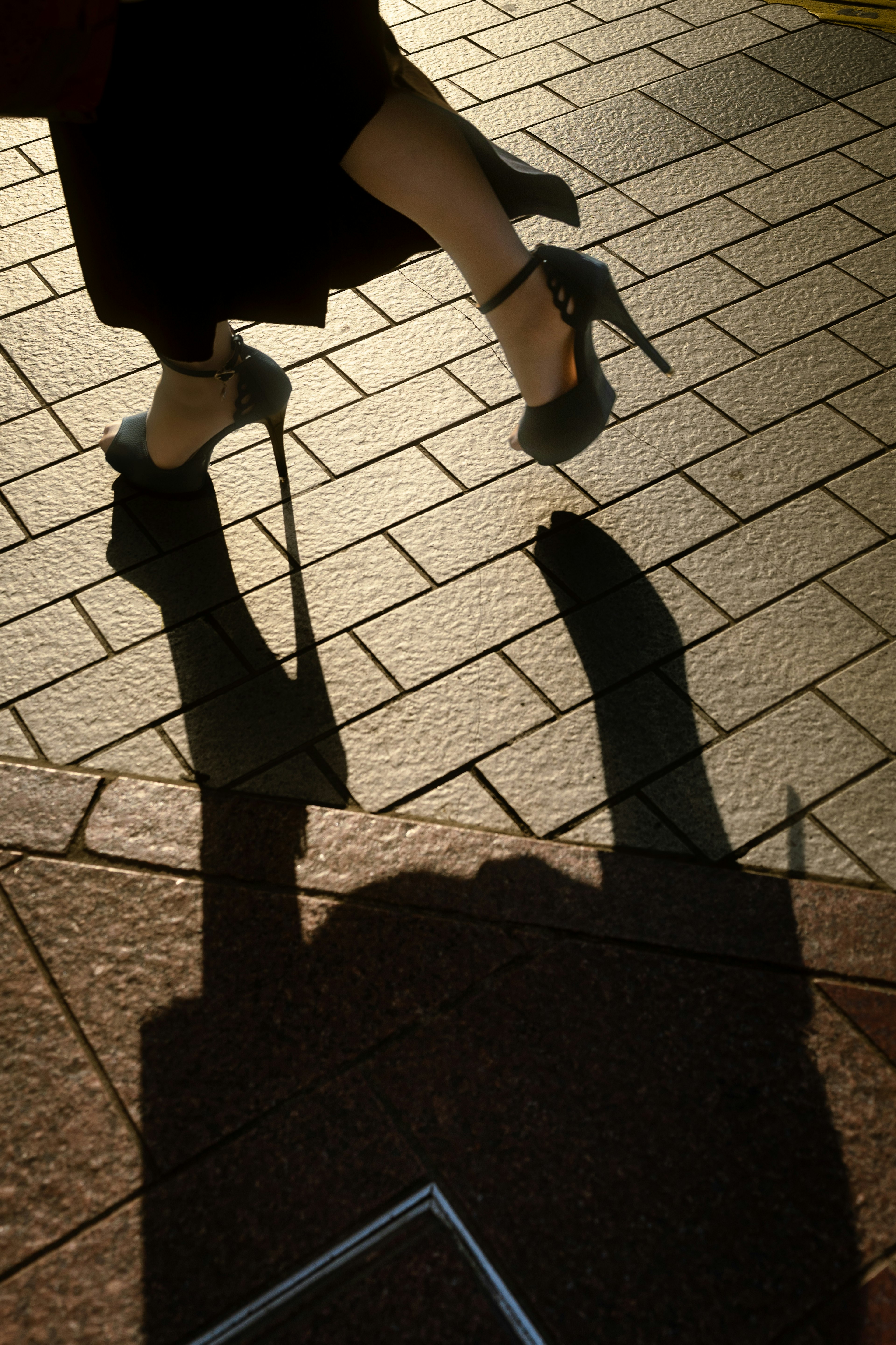 A woman's feet in high heels casting a shadow on the pavement