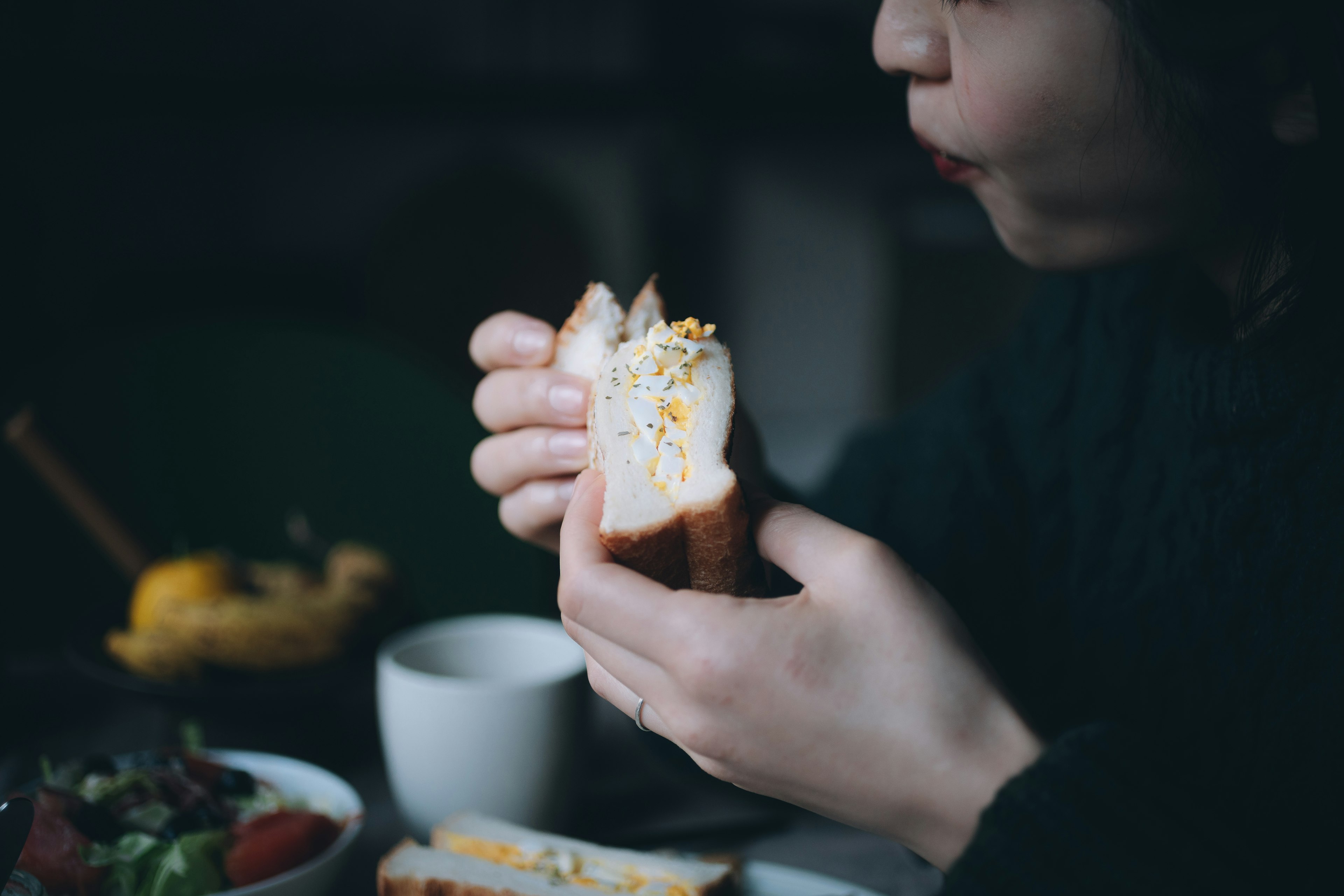 Seorang wanita sedang makan sandwich dengan salad dan cangkir di atas meja