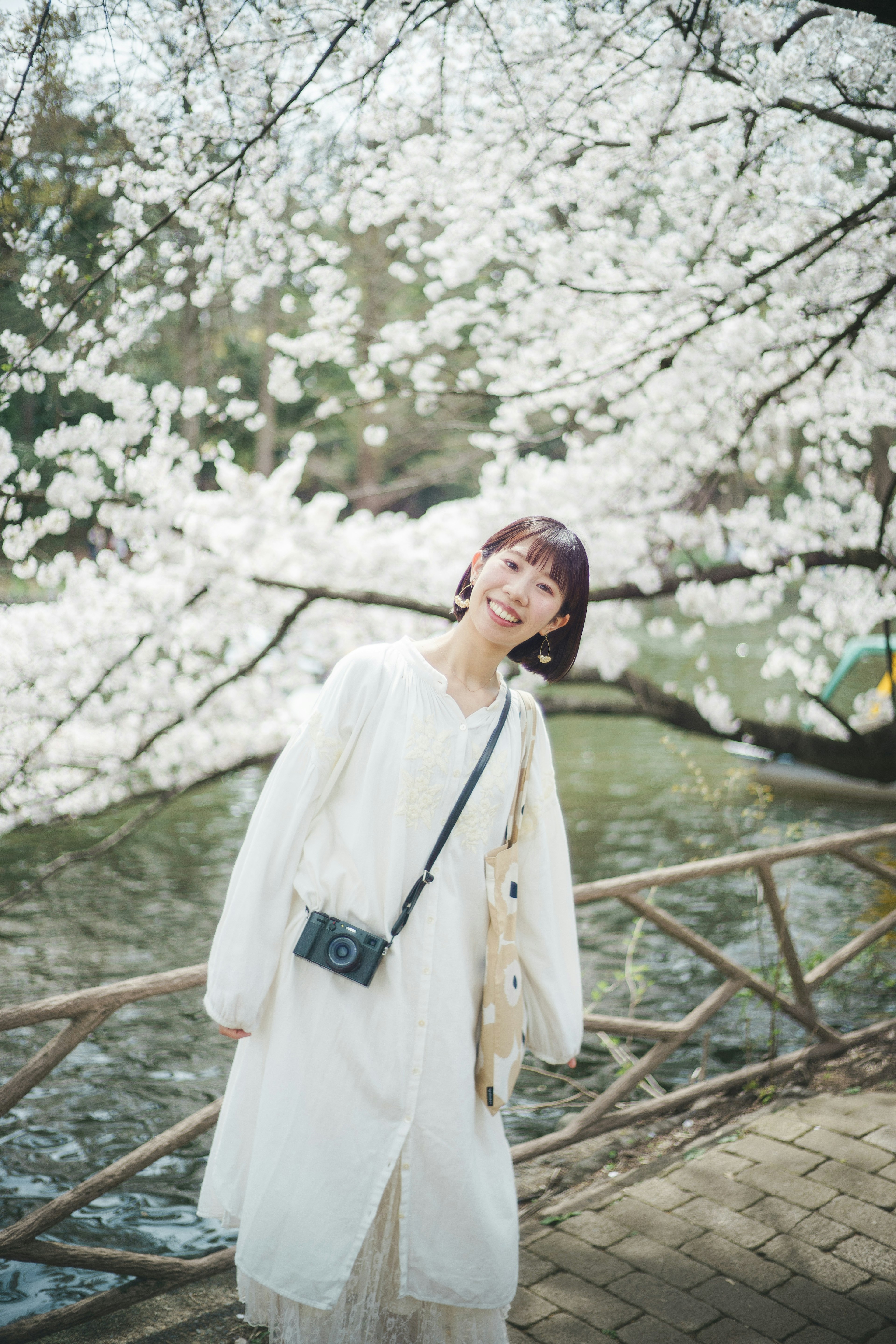 Une femme en tenue blanche souriant sous un cerisier en fleurs