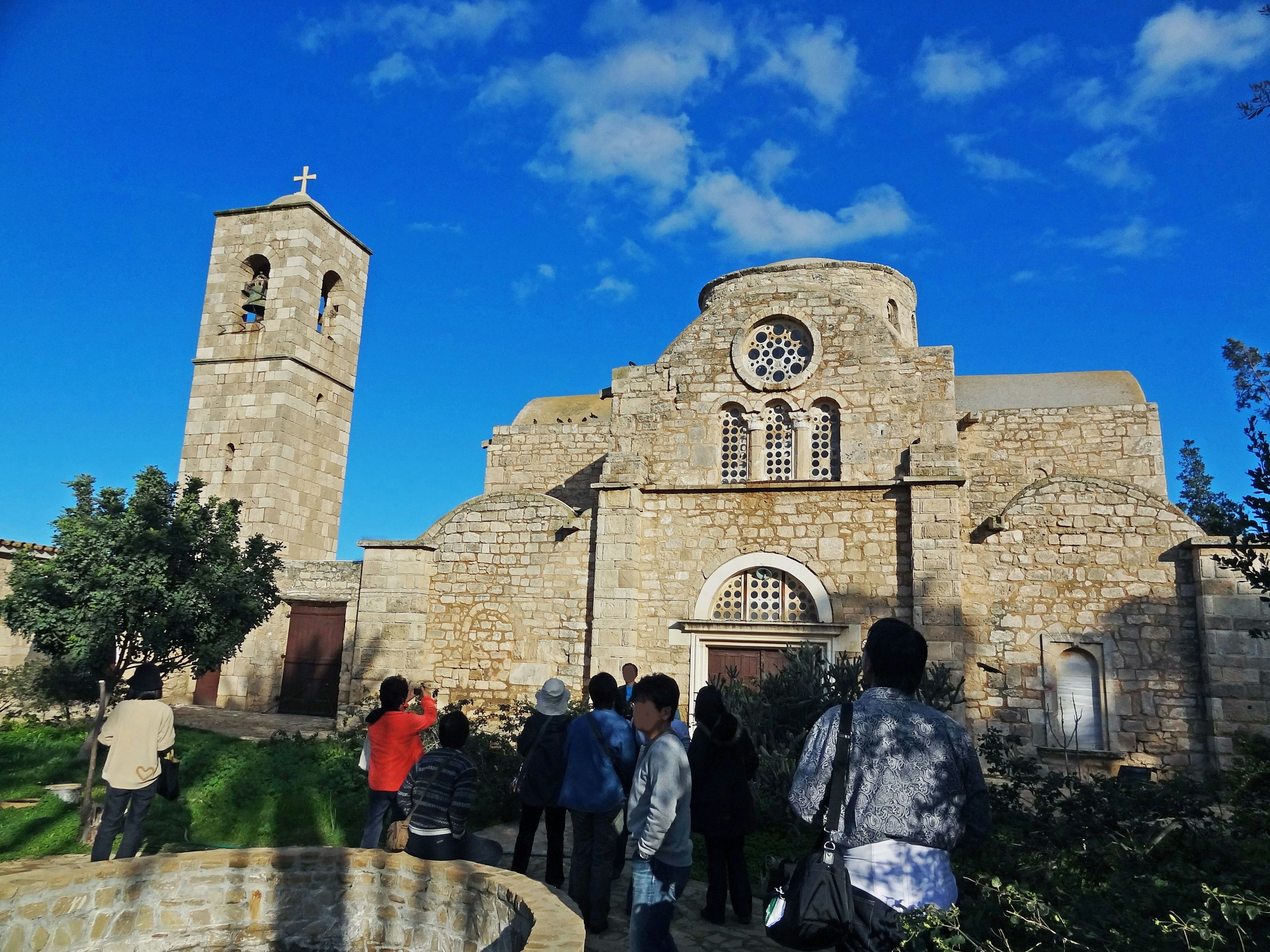 Chiesa in pietra con campanile e un gruppo di turisti sotto un cielo blu