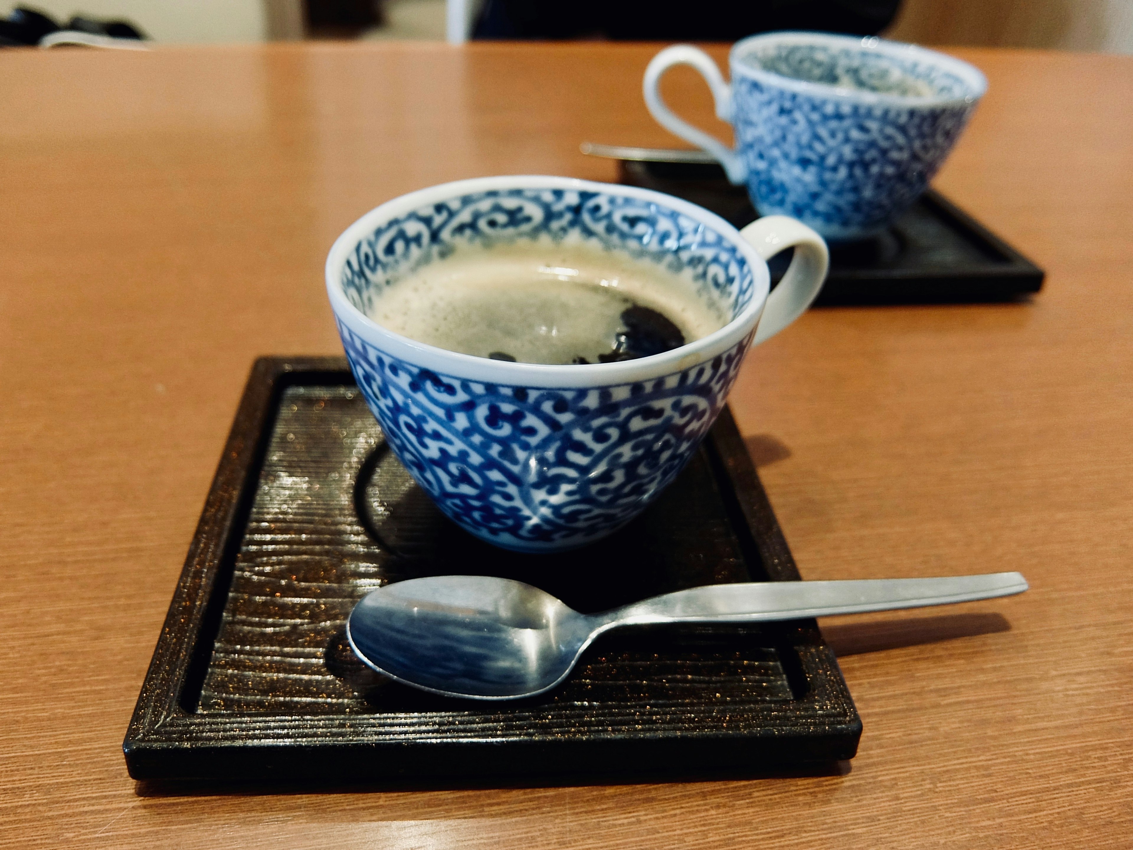 Coffee in a blue patterned cup with a spoon on a wooden tray