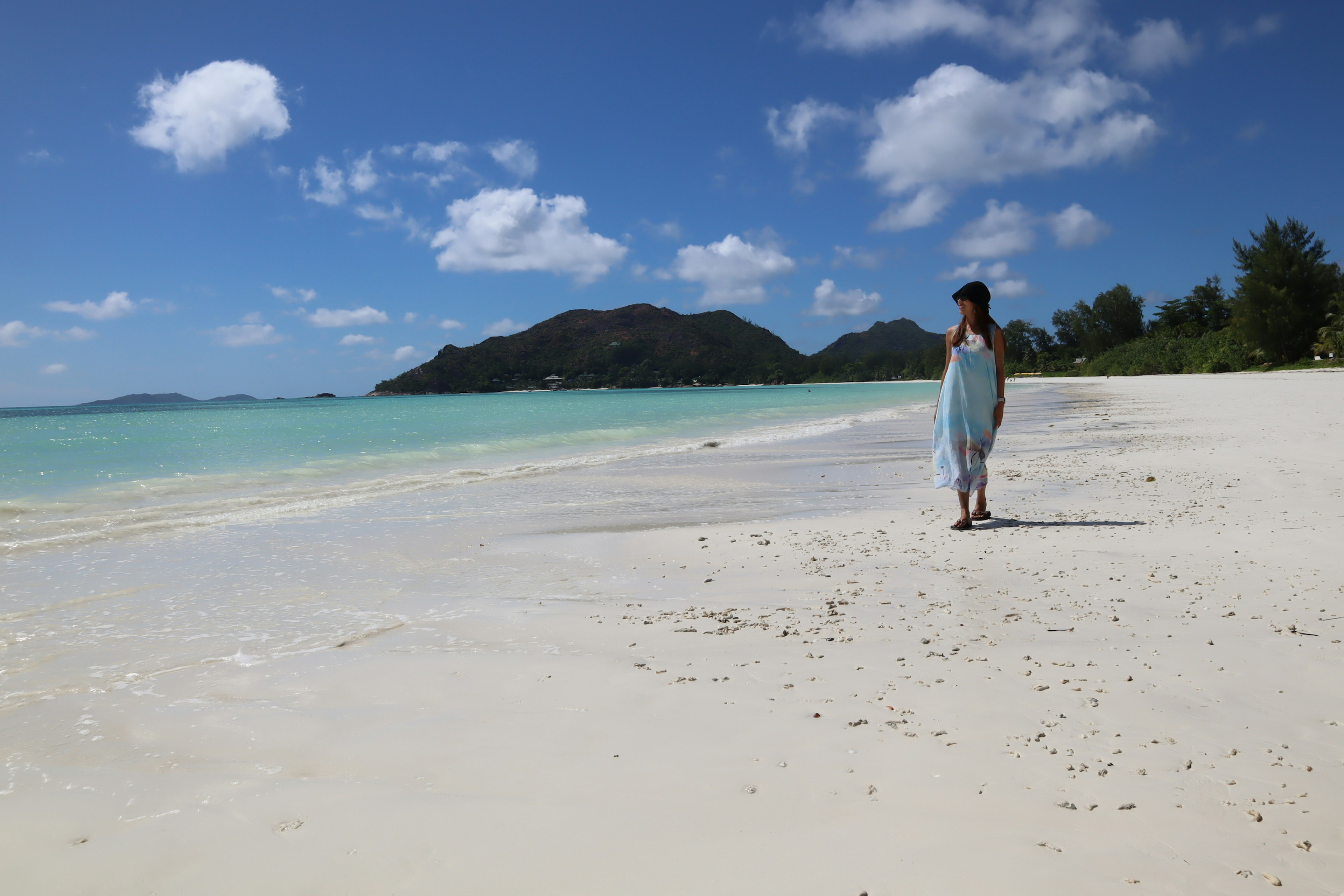 A woman walking on a white sandy beach with turquoise water and blue sky