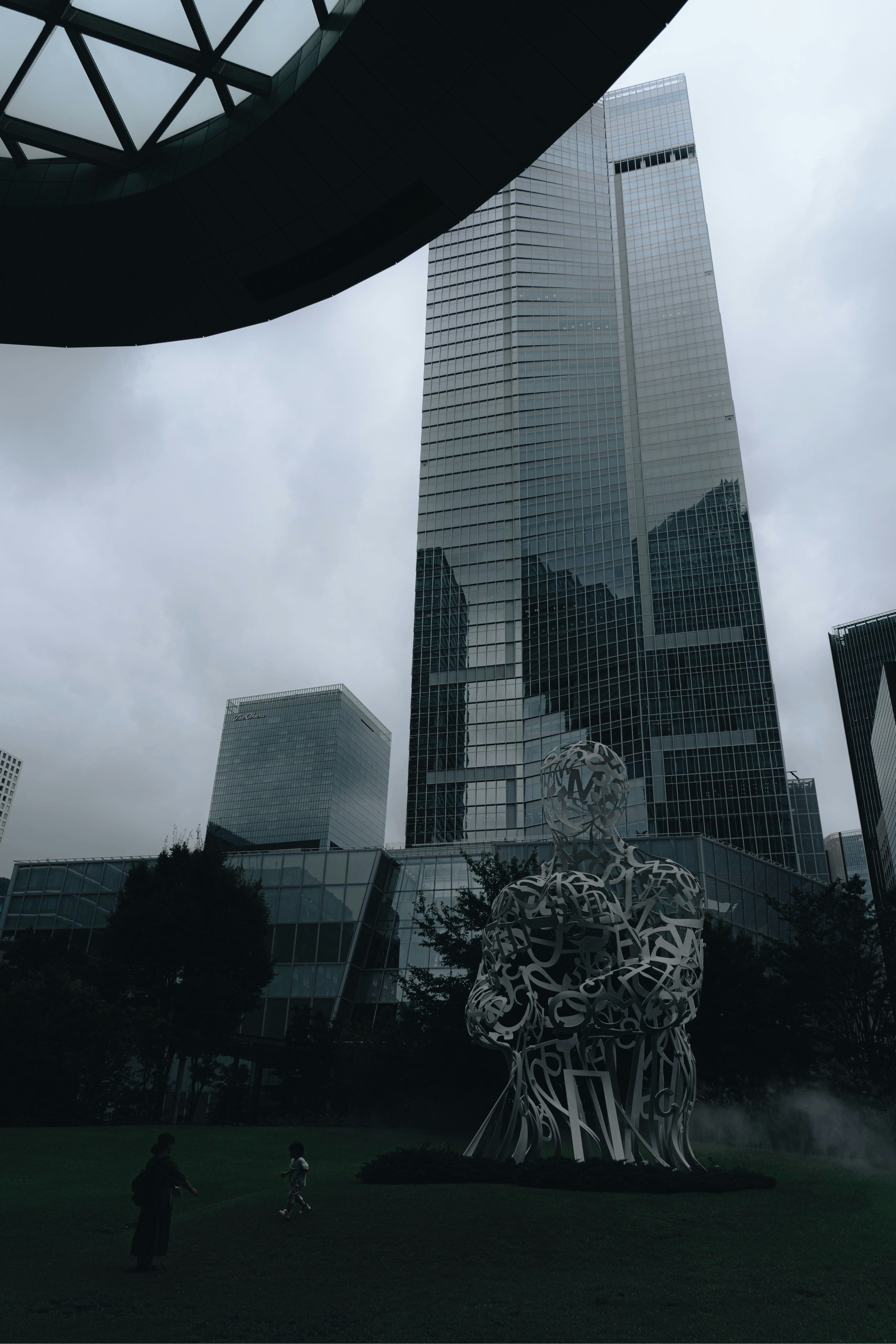 View of a modern skyscraper with a white sculpture in a park