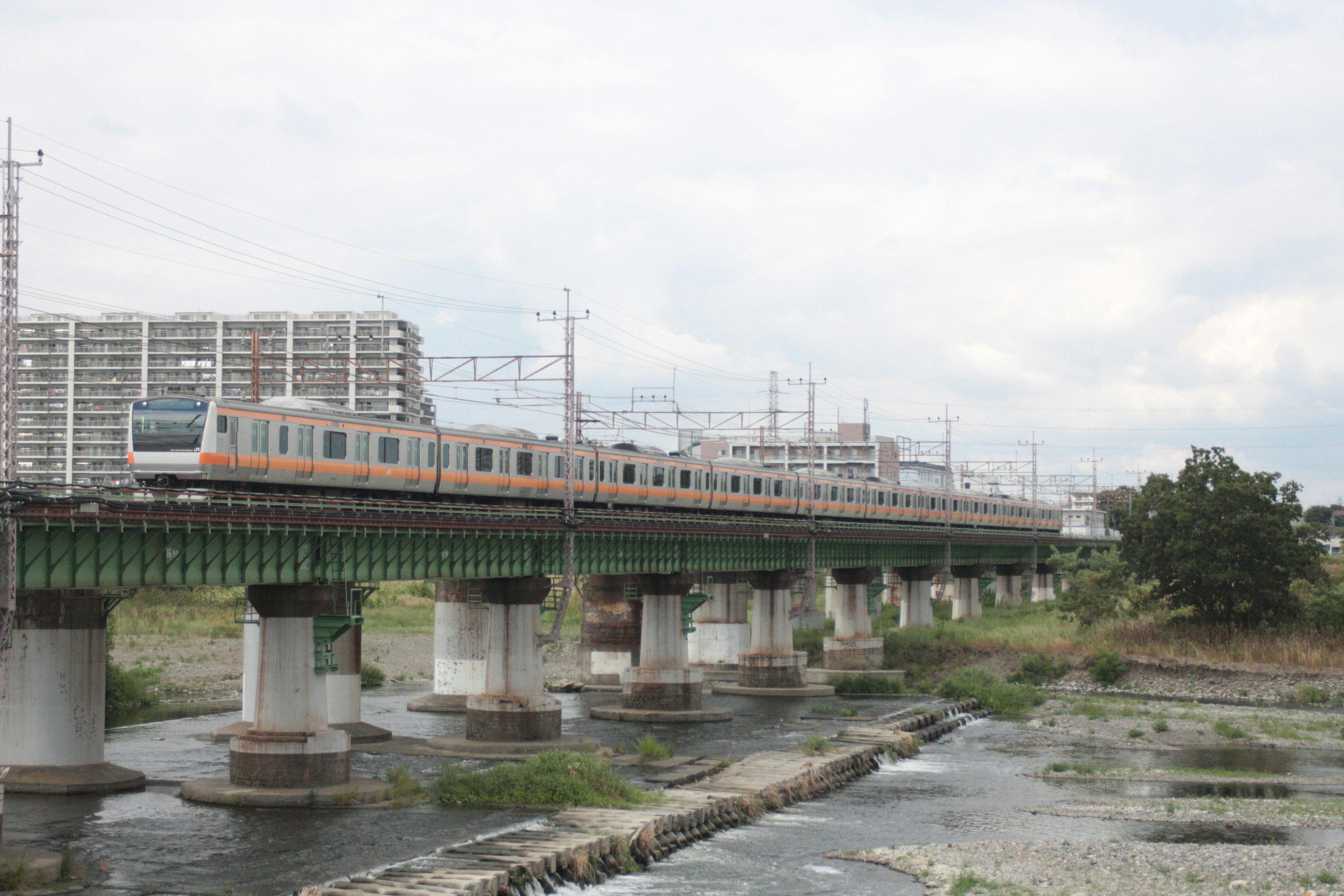 Train crossing a river on an elevated bridge with surrounding buildings