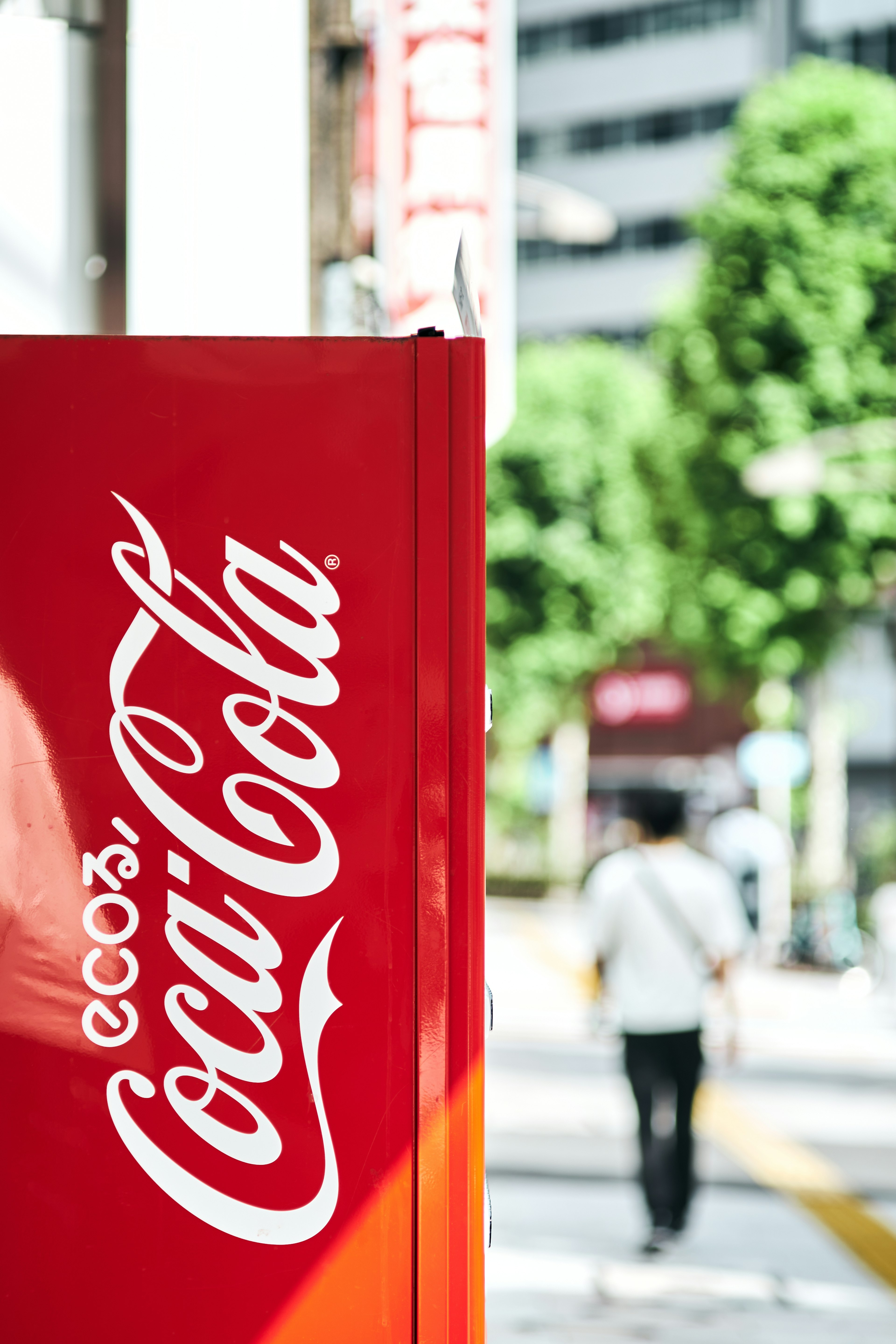 Mesin penjual otomatis Coca-Cola merah dengan orang di latar belakang