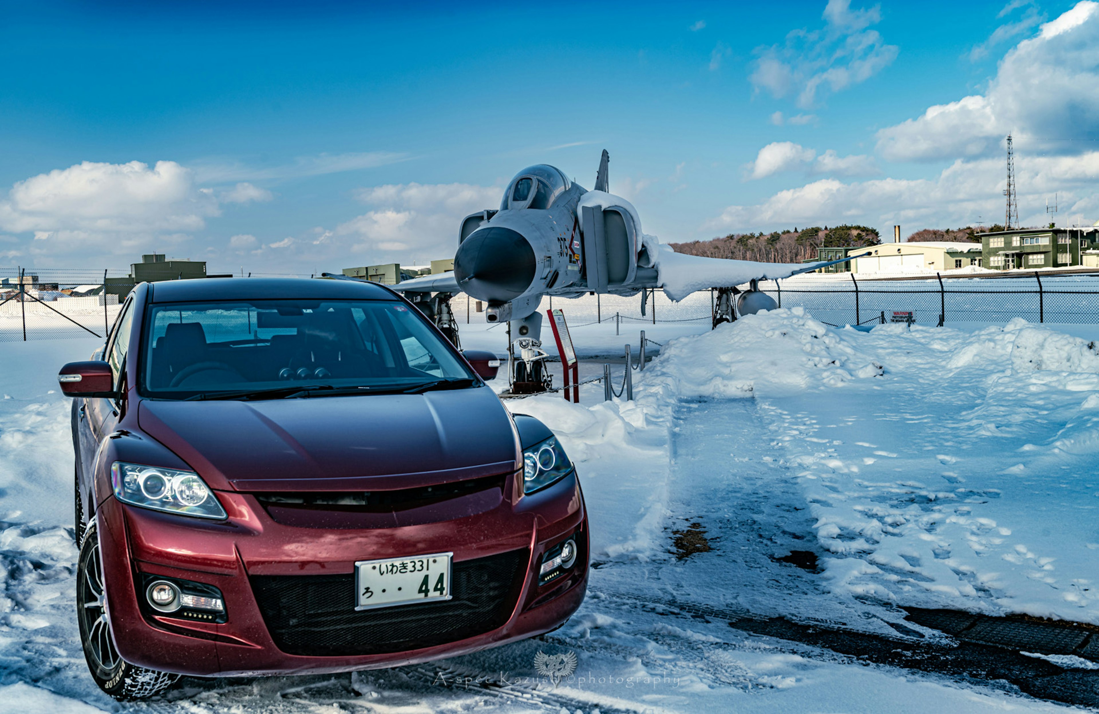 Red car parked in a snowy landscape with an aircraft in the background