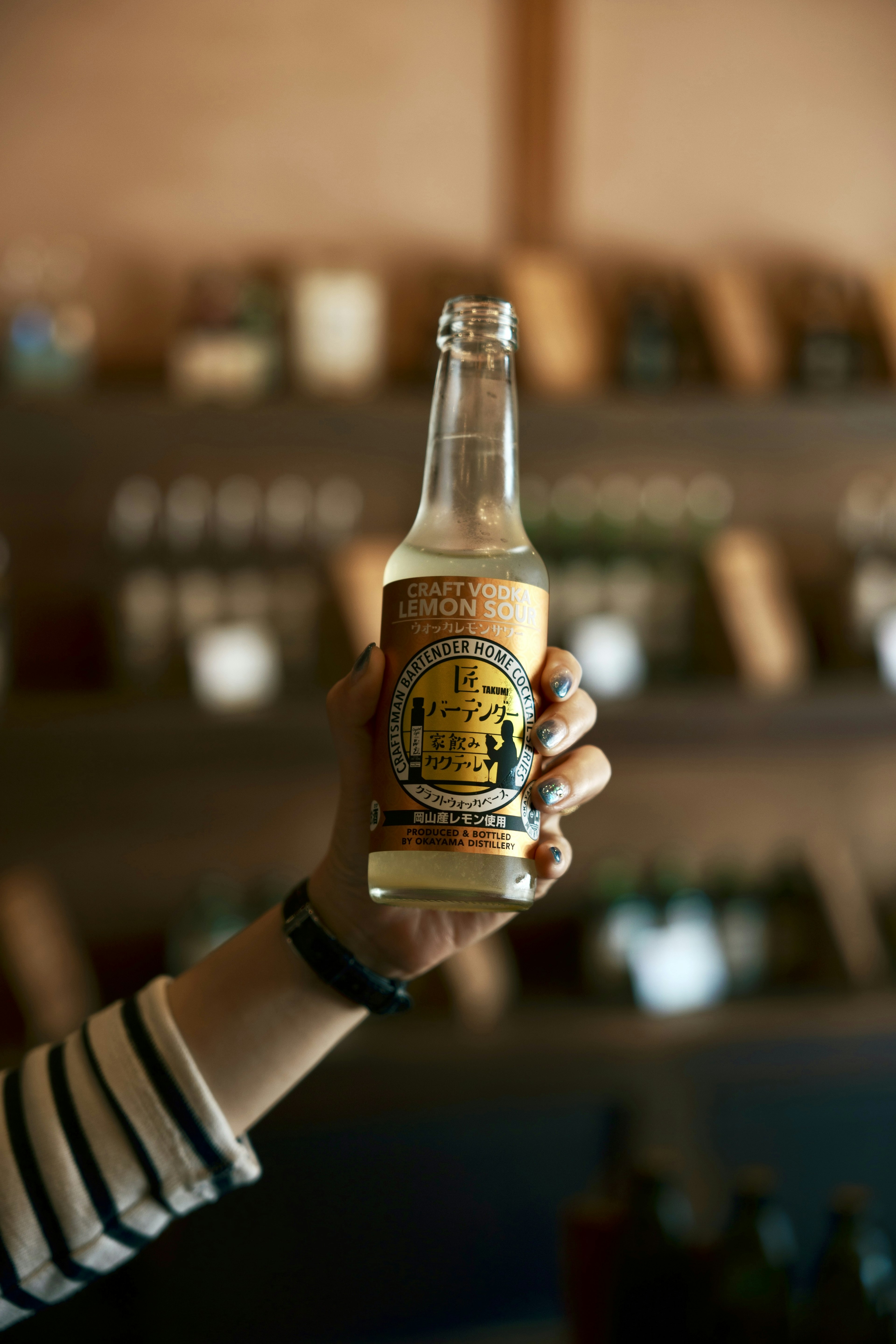 A hand holding a bottle with a label against a background of shelves filled with bottles