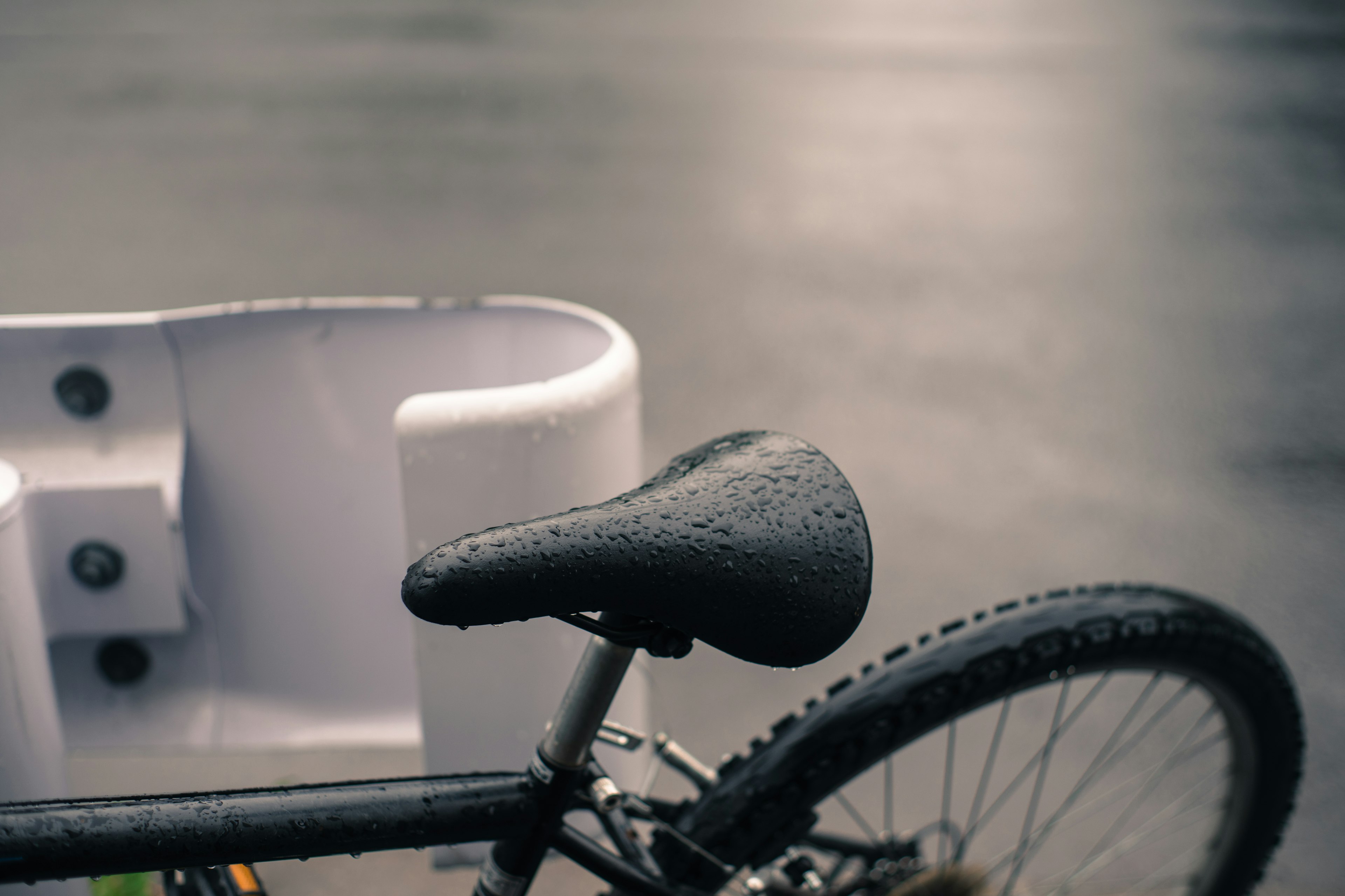 Wet bicycle seat with a white basket in the background