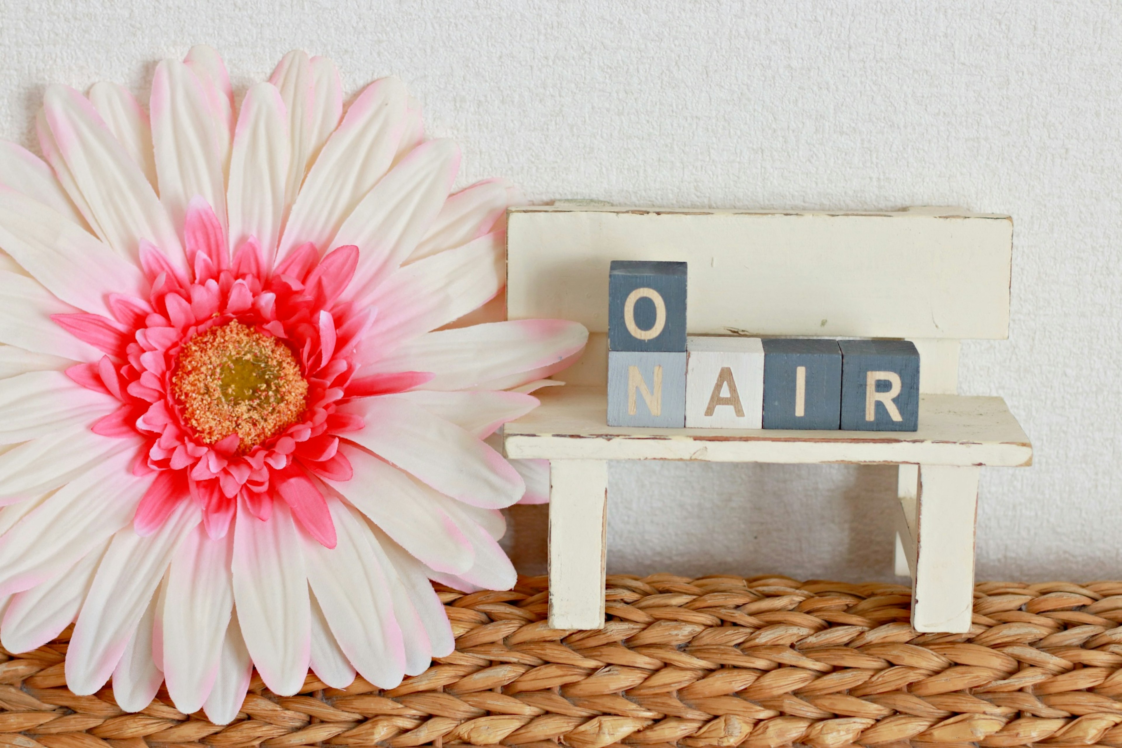 Petit banc blanc avec des lettres en blocs écrivant O N A I R et une fleur rose