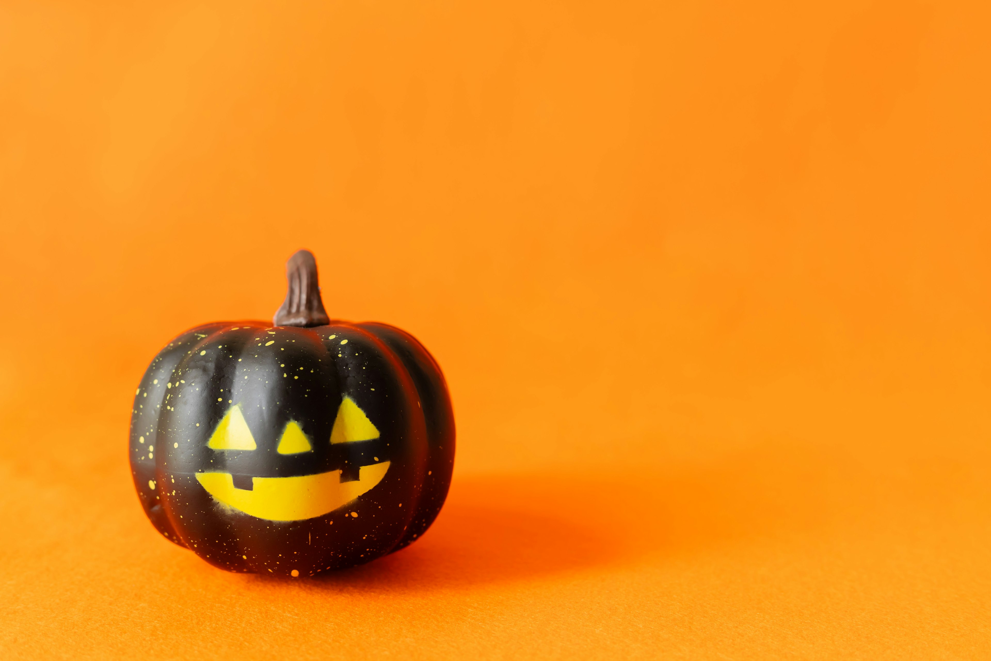 Black Halloween pumpkin with yellow face on orange background