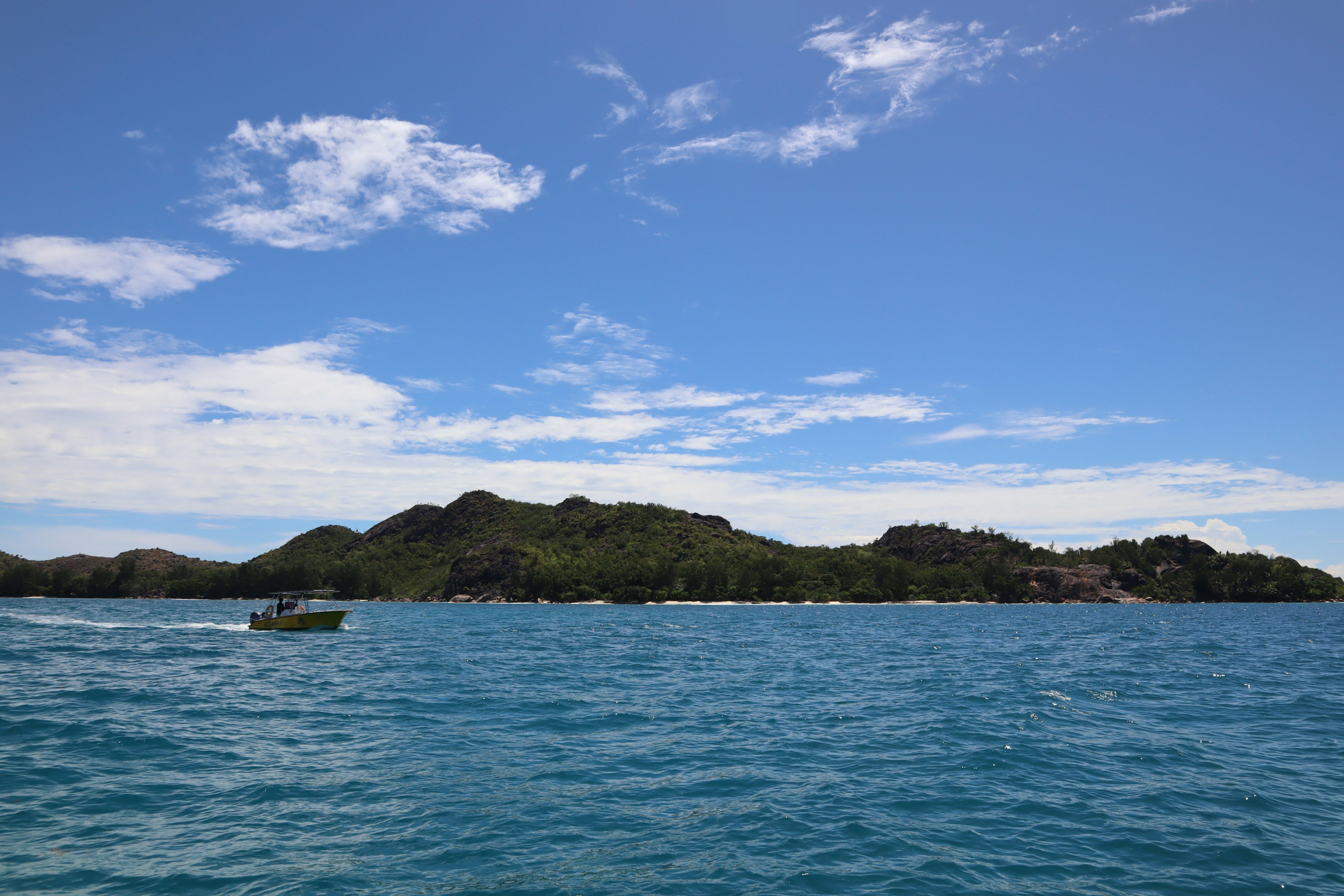 Eine grüne Insel unter einem blauen Himmel mit einem Boot im türkisfarbenen Meer