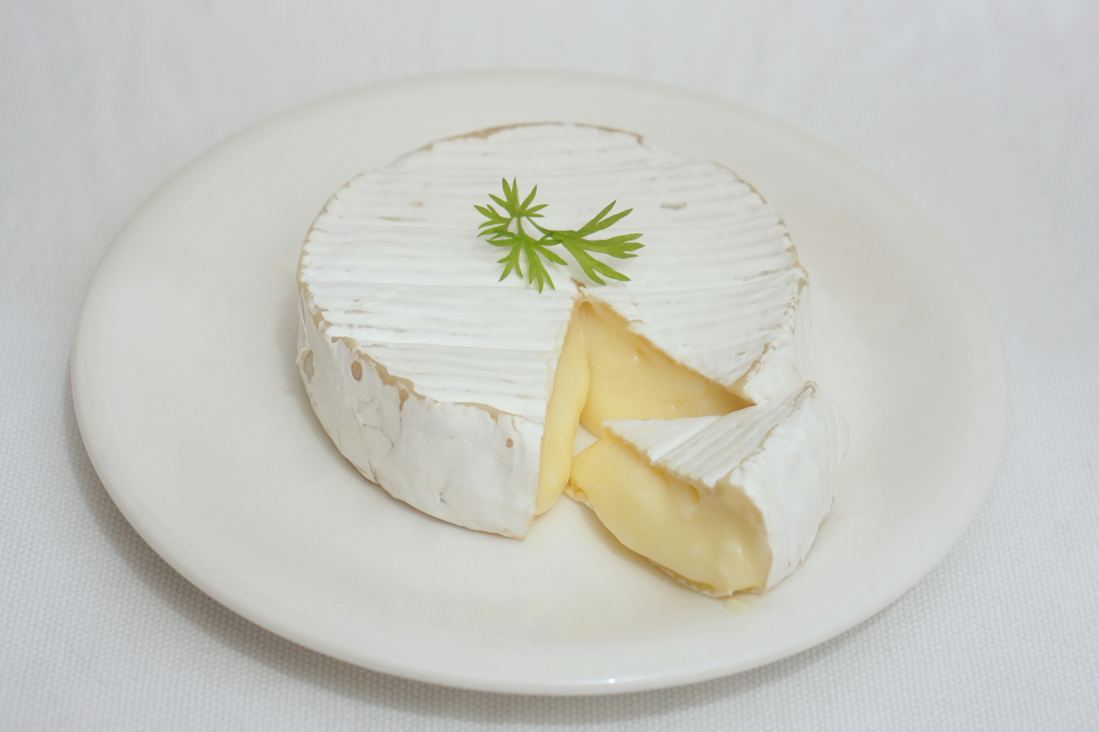 Un formaggio Camembert tondo con una fetta tagliata e guarnito con prezzemolo