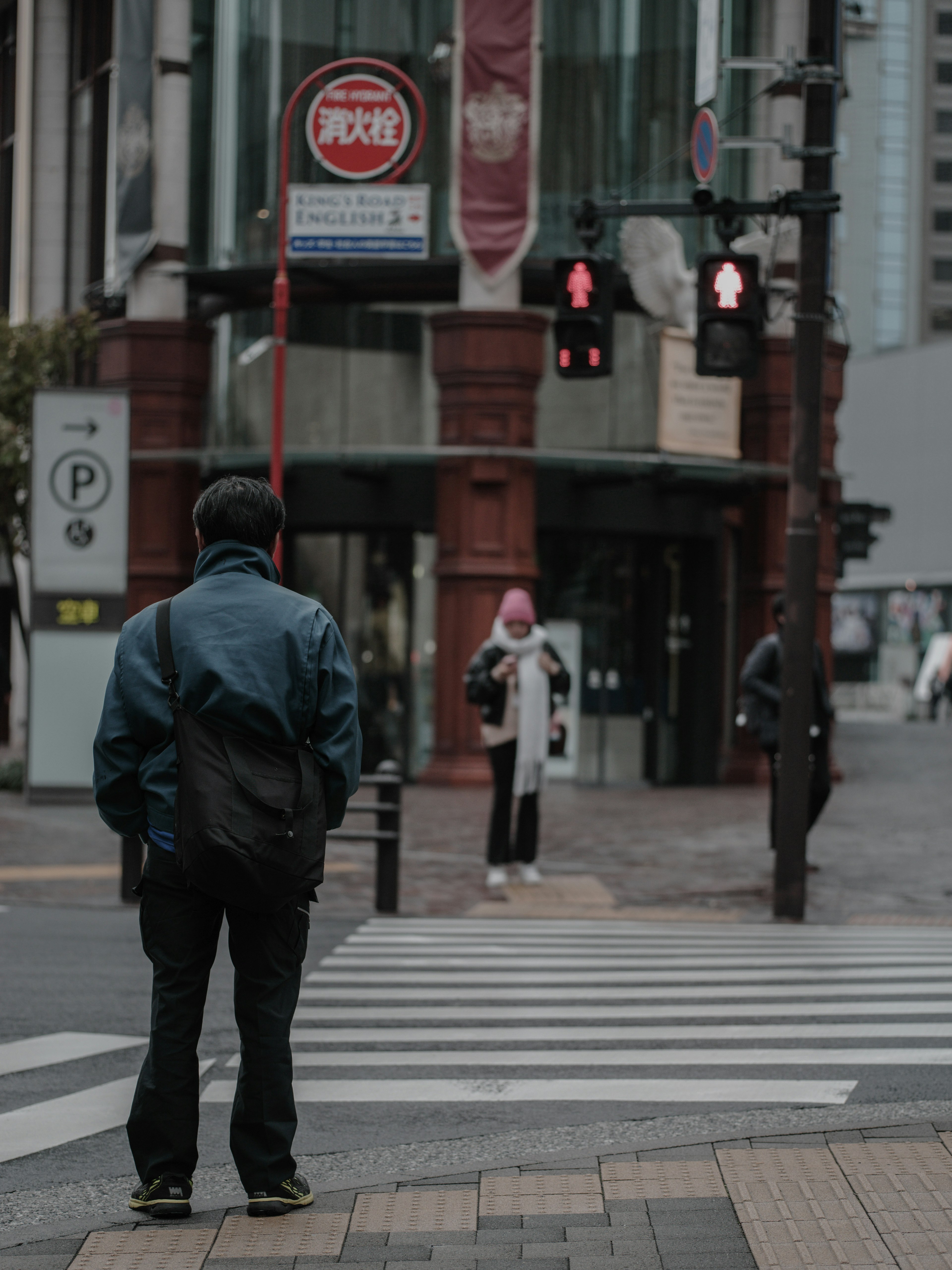 Hombre esperando en un cruce peatonal con una mujer al fondo