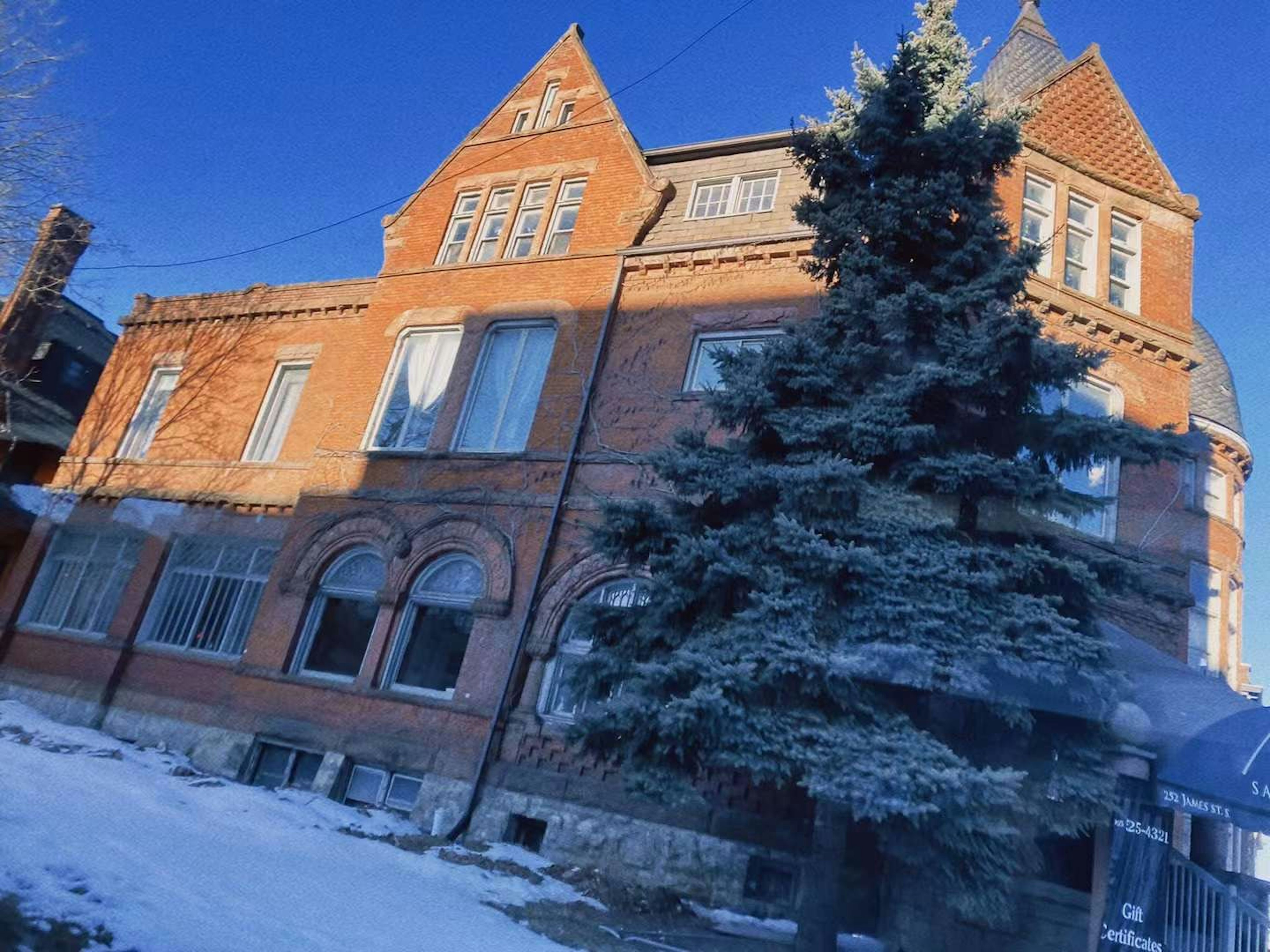 Historic brick house with snow-covered yard and evergreen tree