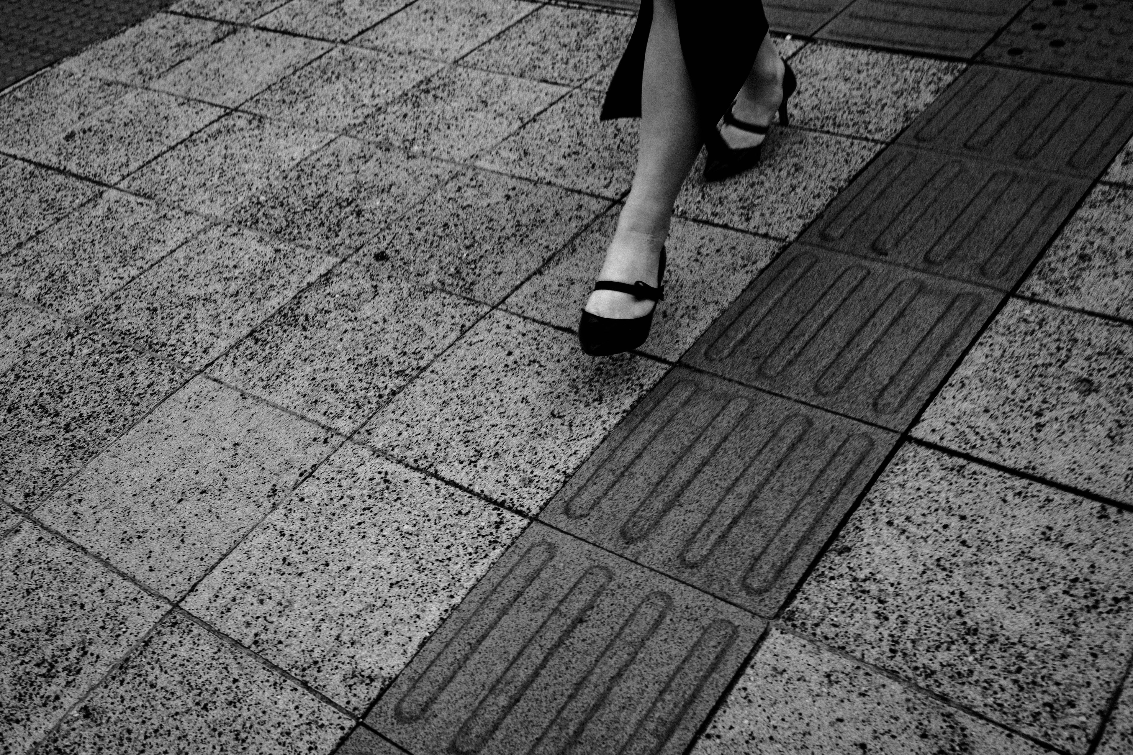 Des pieds de femme en chaussures noires marchant sur un pavé texturé en noir et blanc