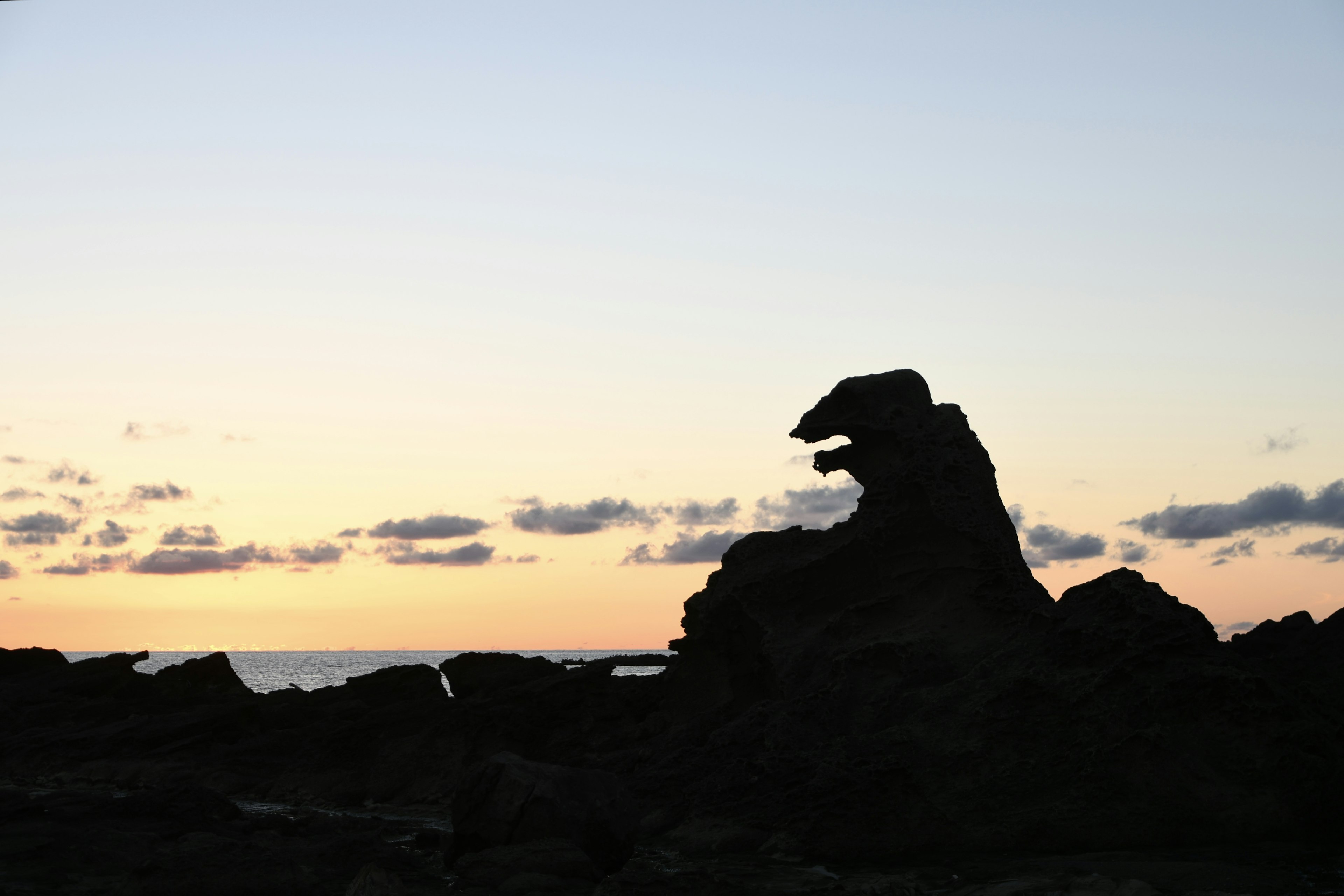 Silhouette di una formazione rocciosa che somiglia a una creatura contro un cielo al tramonto