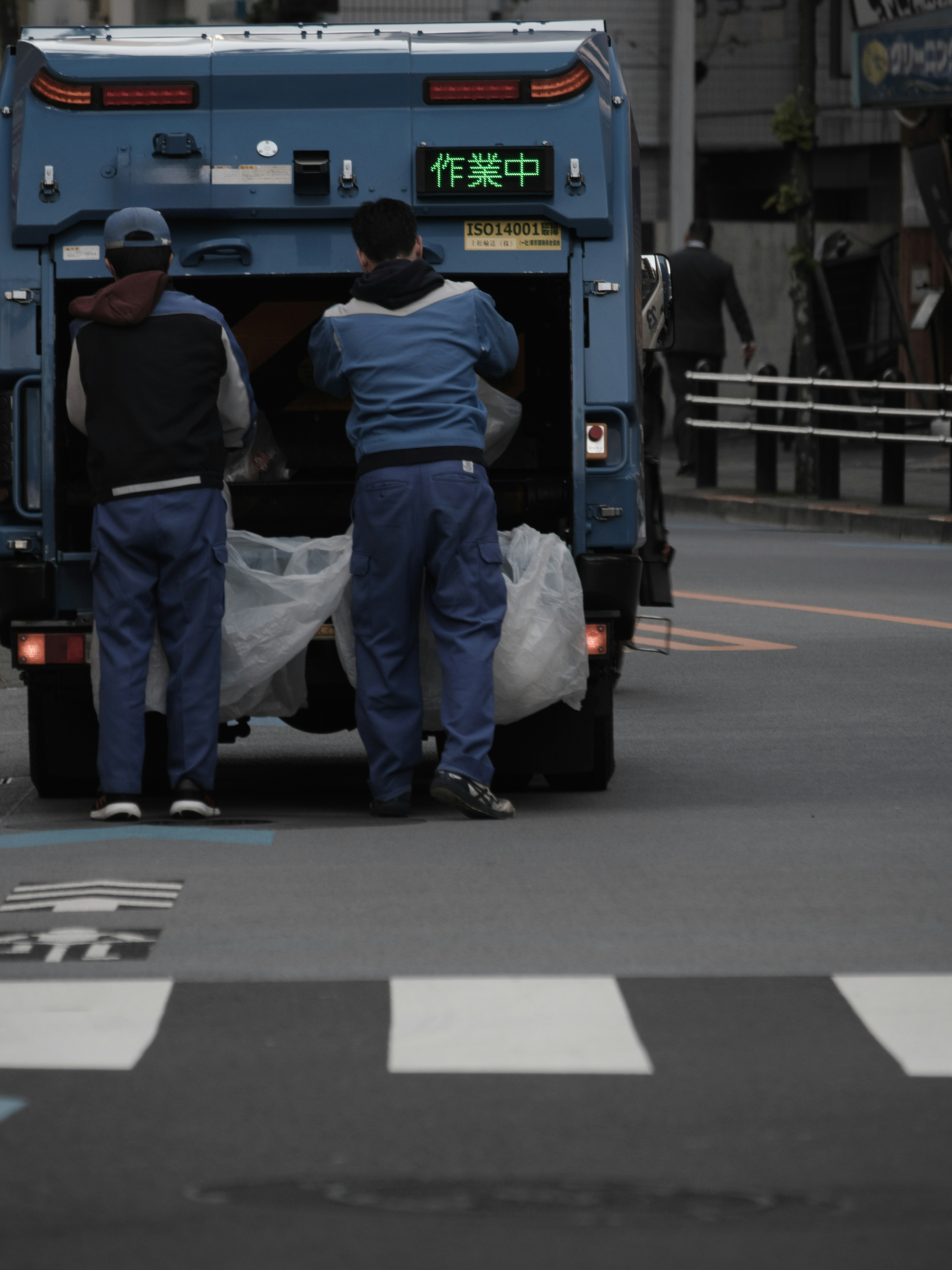 Dos trabajadores operando en la parte trasera de un camión de basura azul