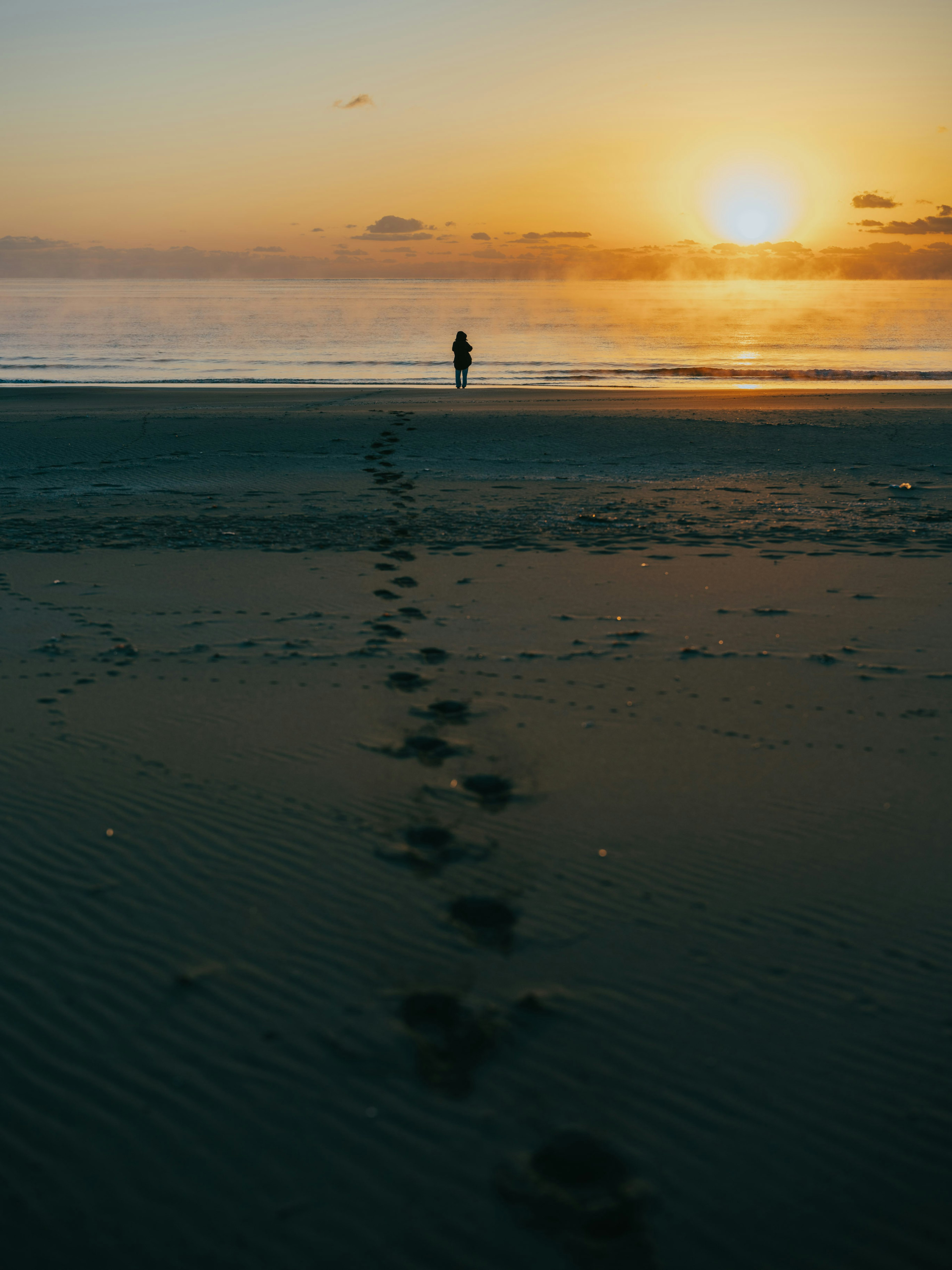 Eine Person, die am Strand läuft, mit Fußspuren, die zum Sonnenuntergang führen