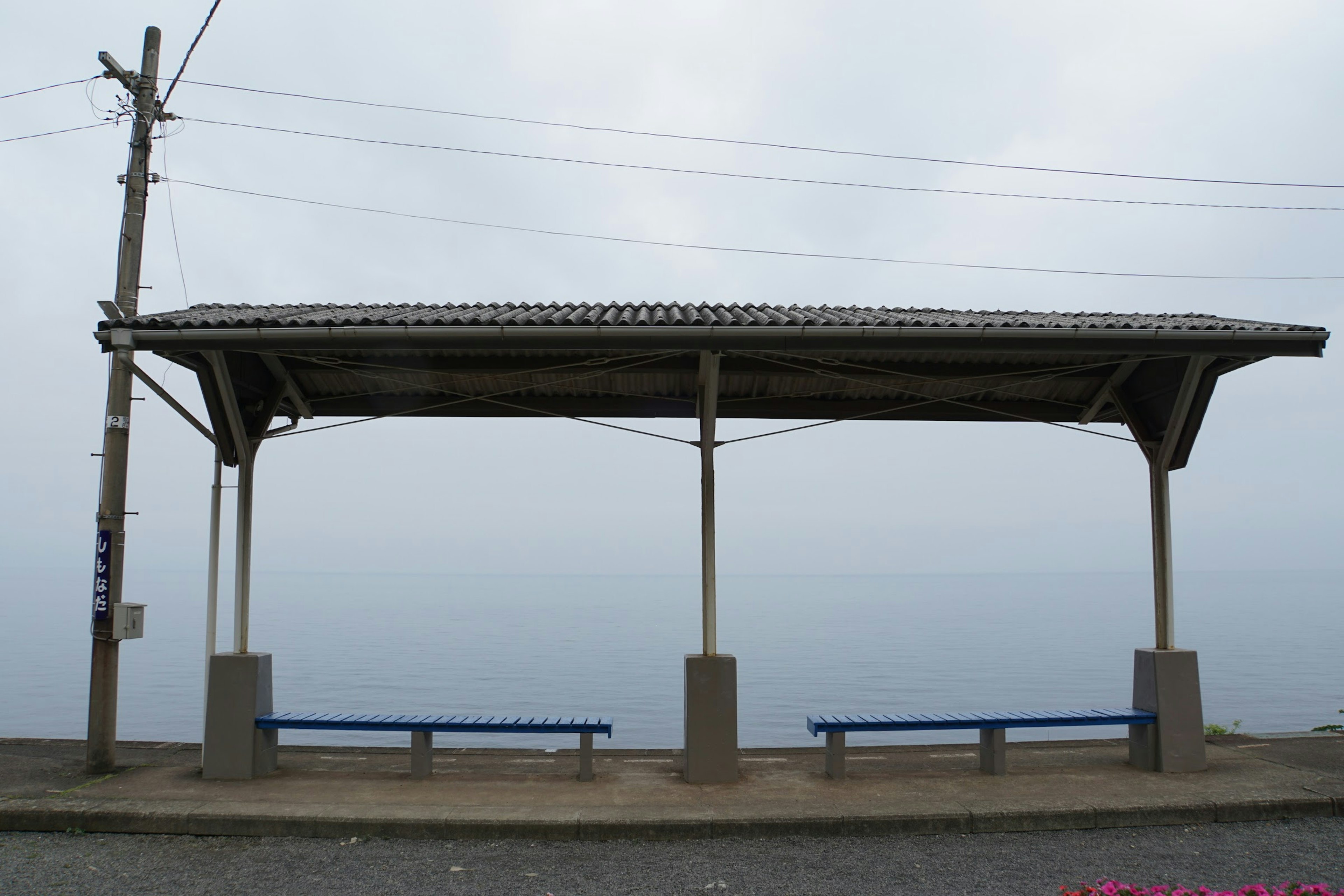 A quiet bus shelter with blue benches and a cloudy sky