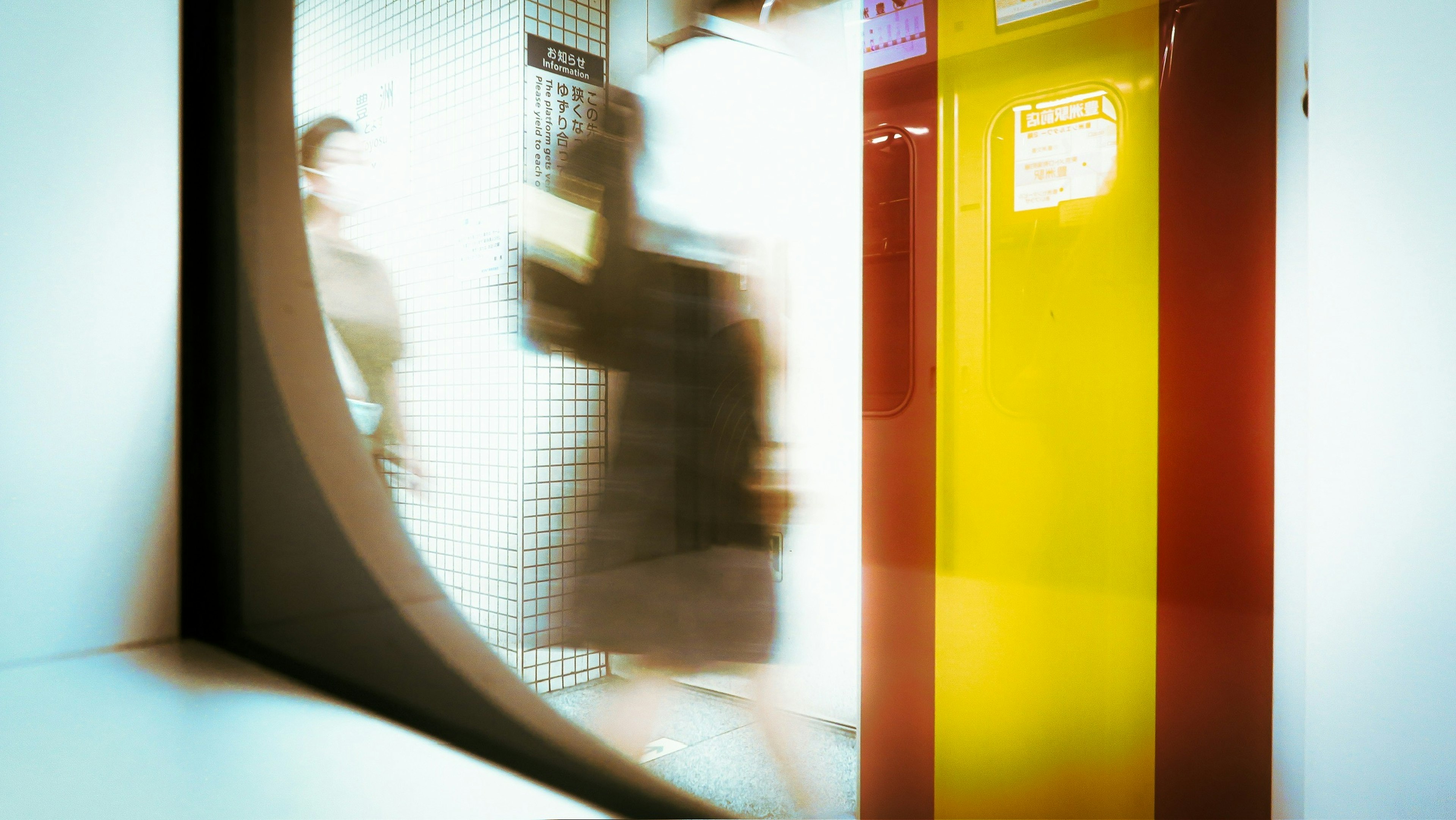 Verschwommene Aufnahme von Menschen in einer Bahnhof mit markanten gelben und roten Säulen