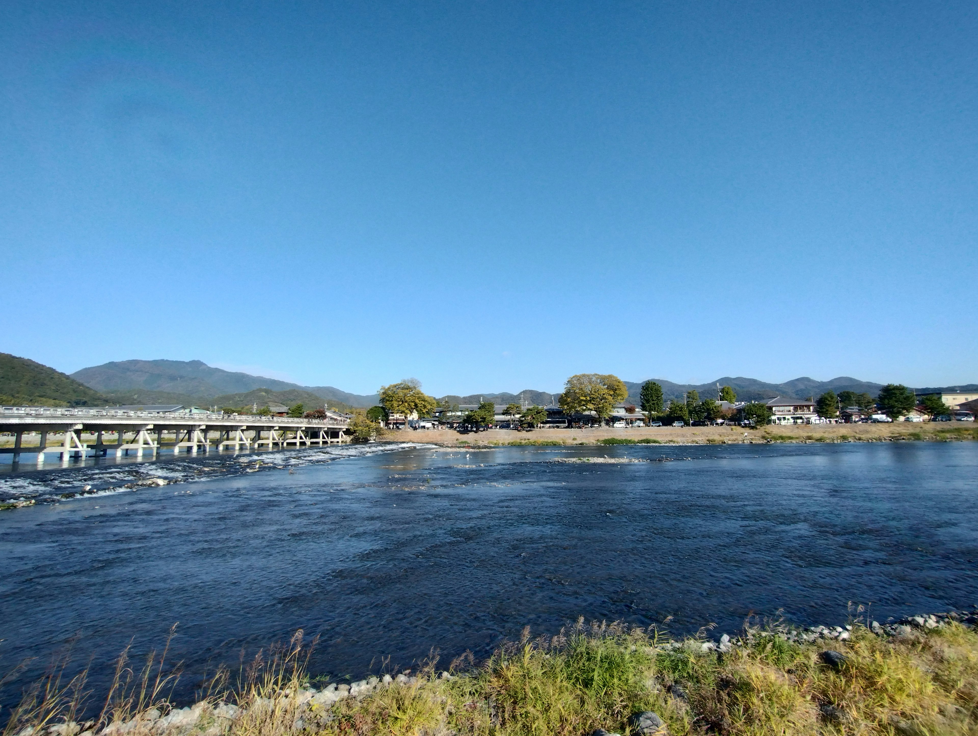 Sungai tenang dengan jembatan dan pegunungan di bawah langit biru yang cerah