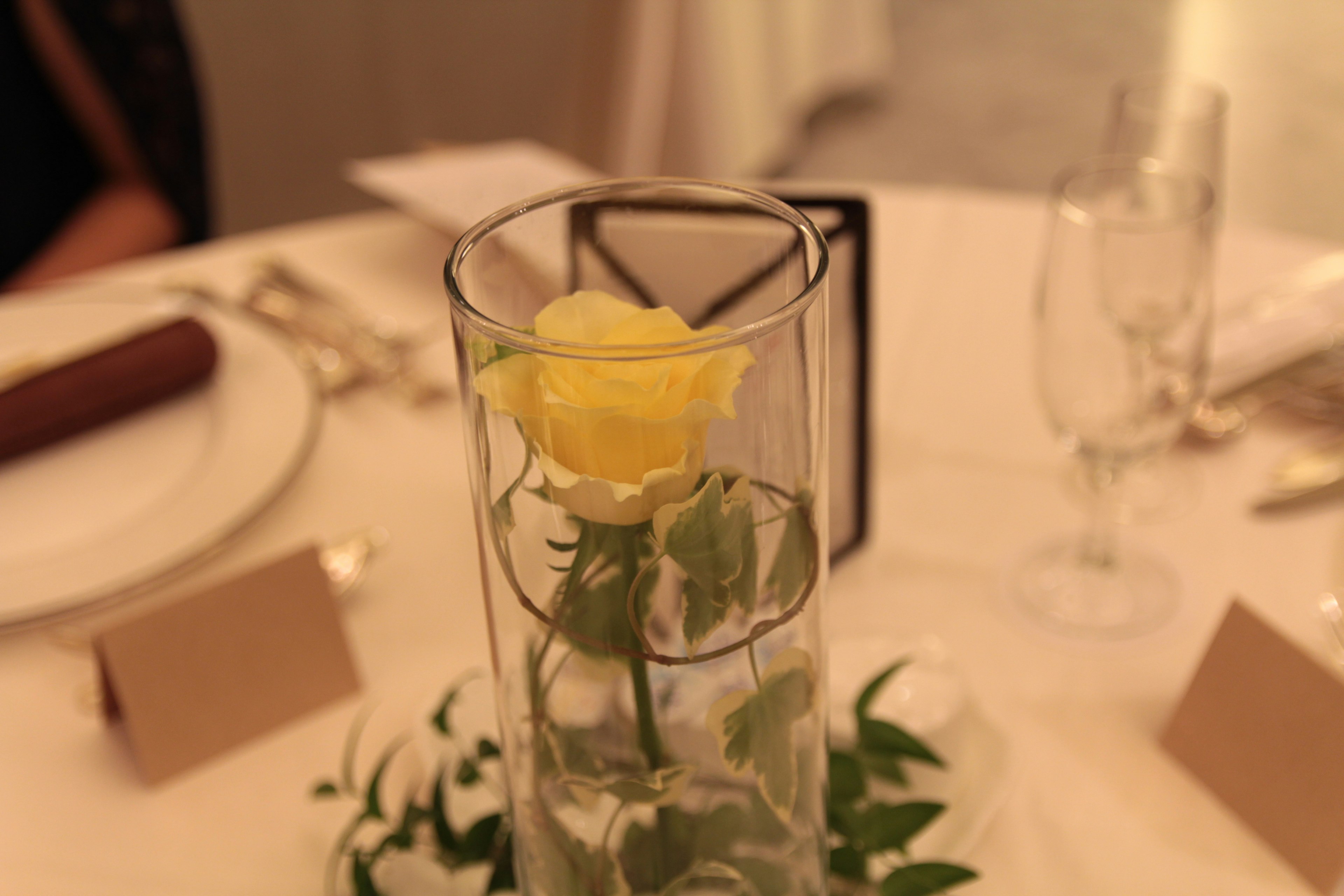 Une rose jaune dans un vase transparent au centre d'une table à manger