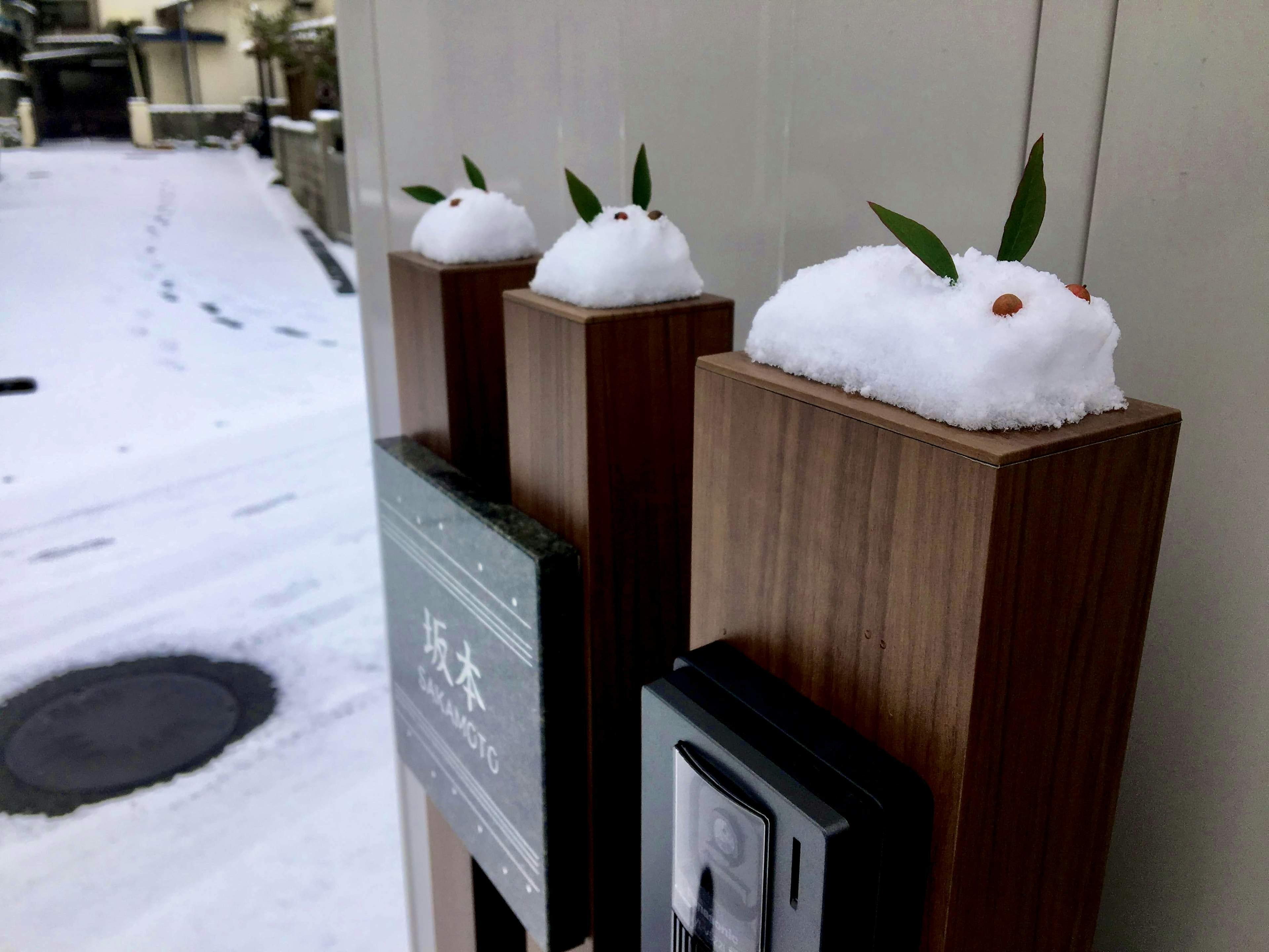 雪で覆われた木のポストに小さな雪の人形と葉が飾られている