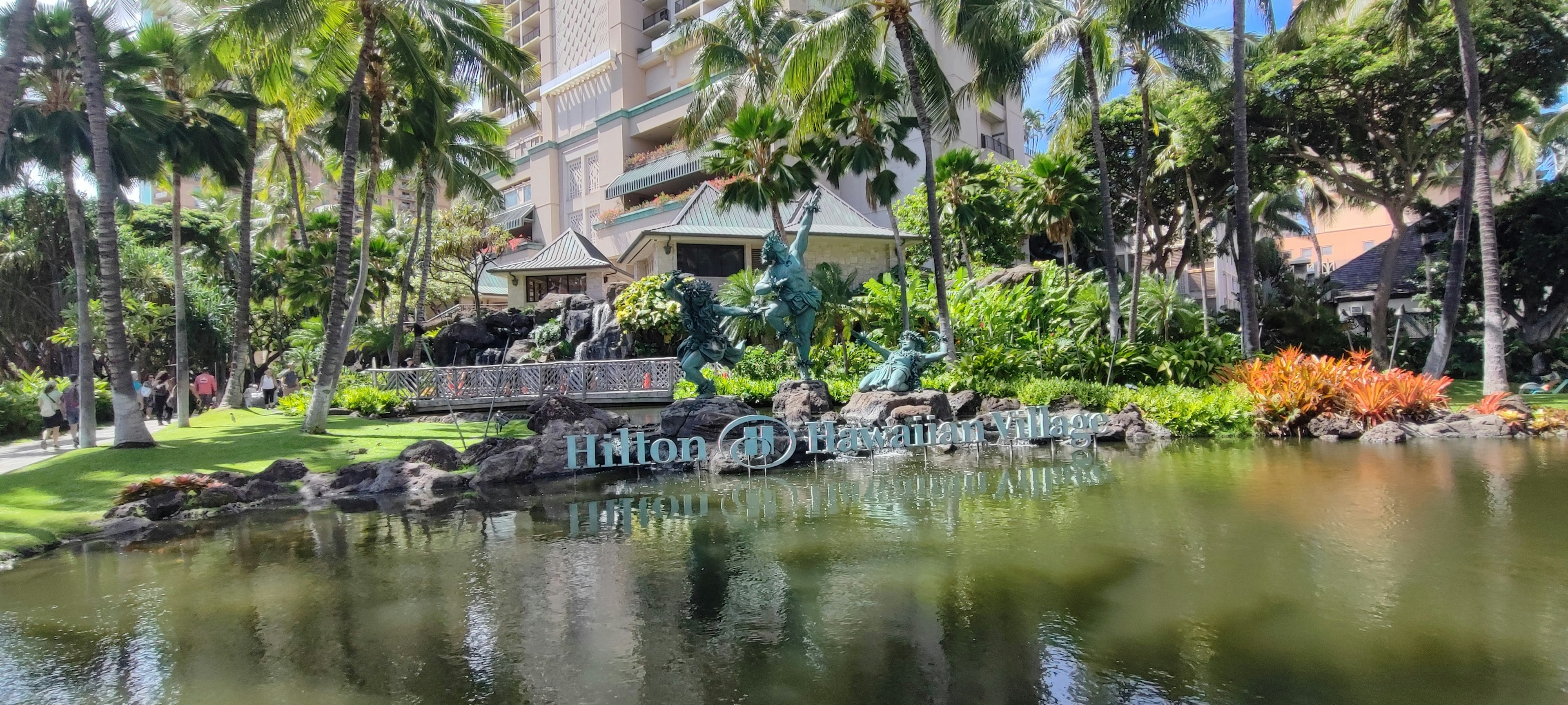 Vista panoramica di uno stagno di giardino tropicale con piante lussureggianti e un edificio